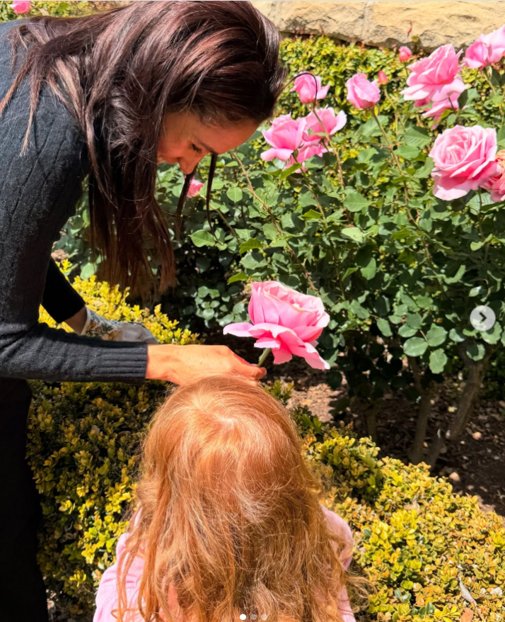 Meghan Markle bends down beside a rose bush as Princess Lilibet admires the vibrant pink blossoms during a quiet garden outing. | Source: Instagram/meghan