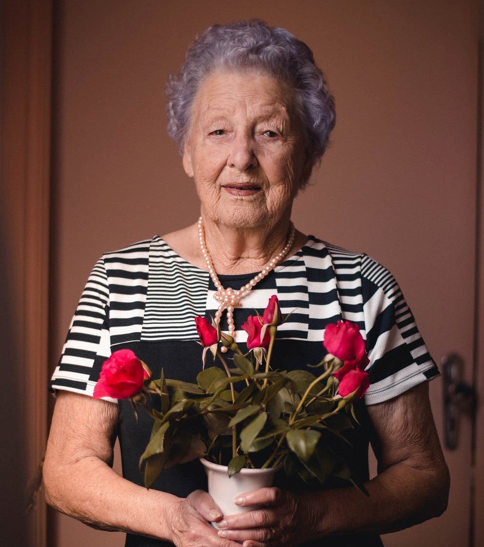 Anciana sonrie mientras sostiene un ramo de rosas entre sus manos. | Foto: Pexels