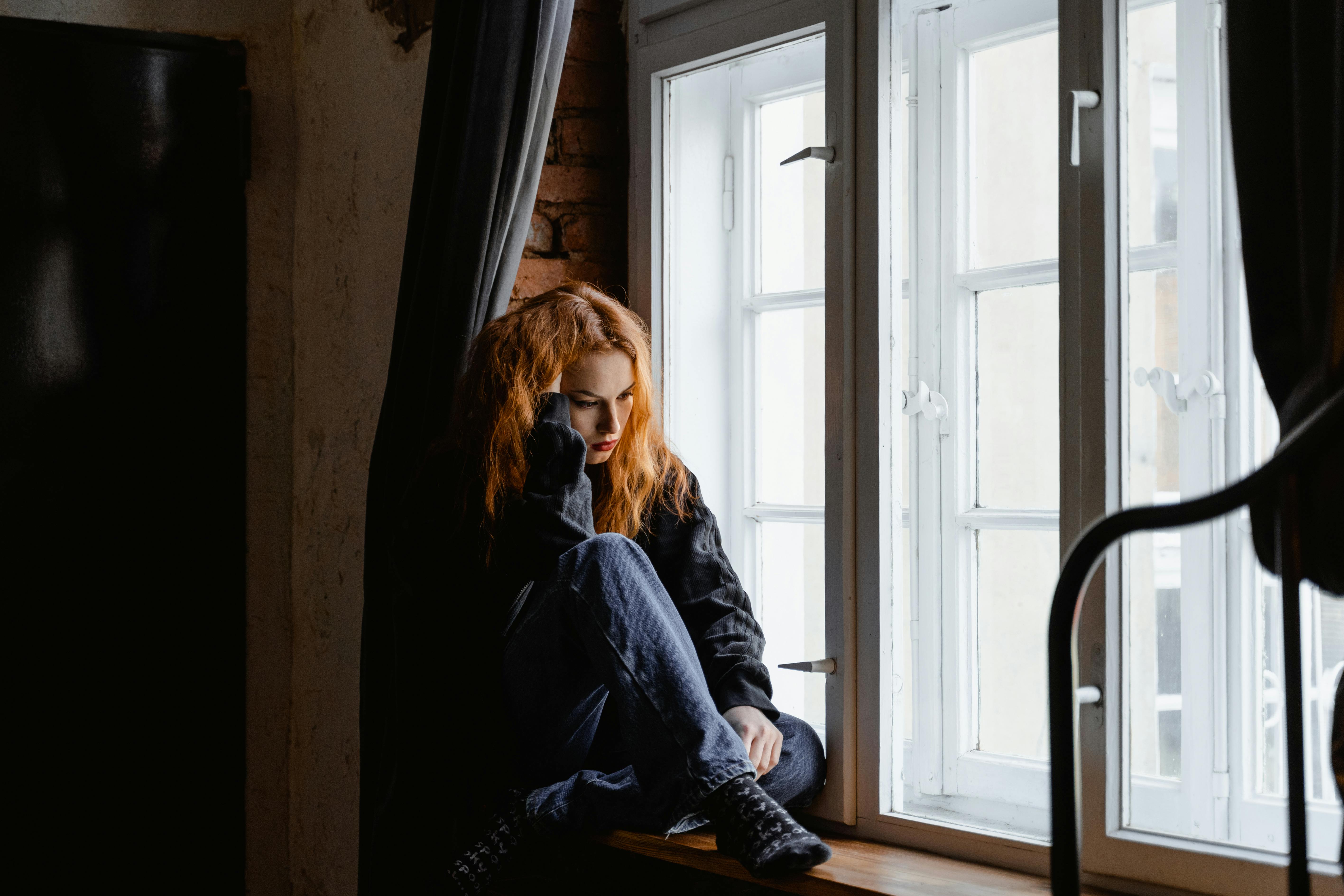 An upset woman sitting on a windowsill | Source: Pexels