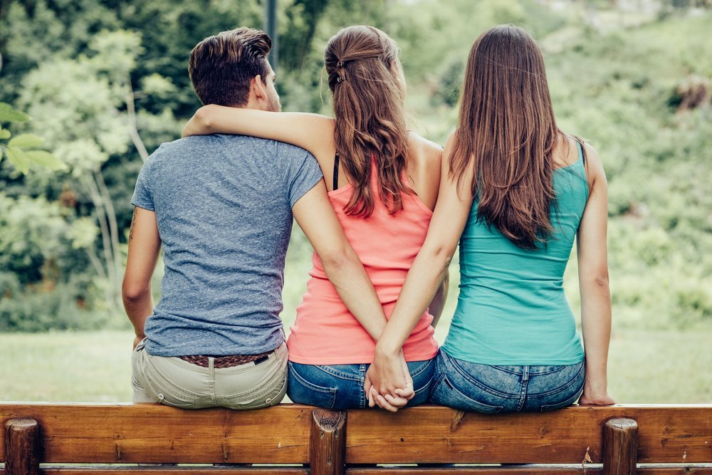 Chica abraza a su novio mientras él toma la mano de otra chica. | Foto: Shutterstock Chica abraza a su novio mientras él toma la mano de otra chica. | Foto: Shutterstock