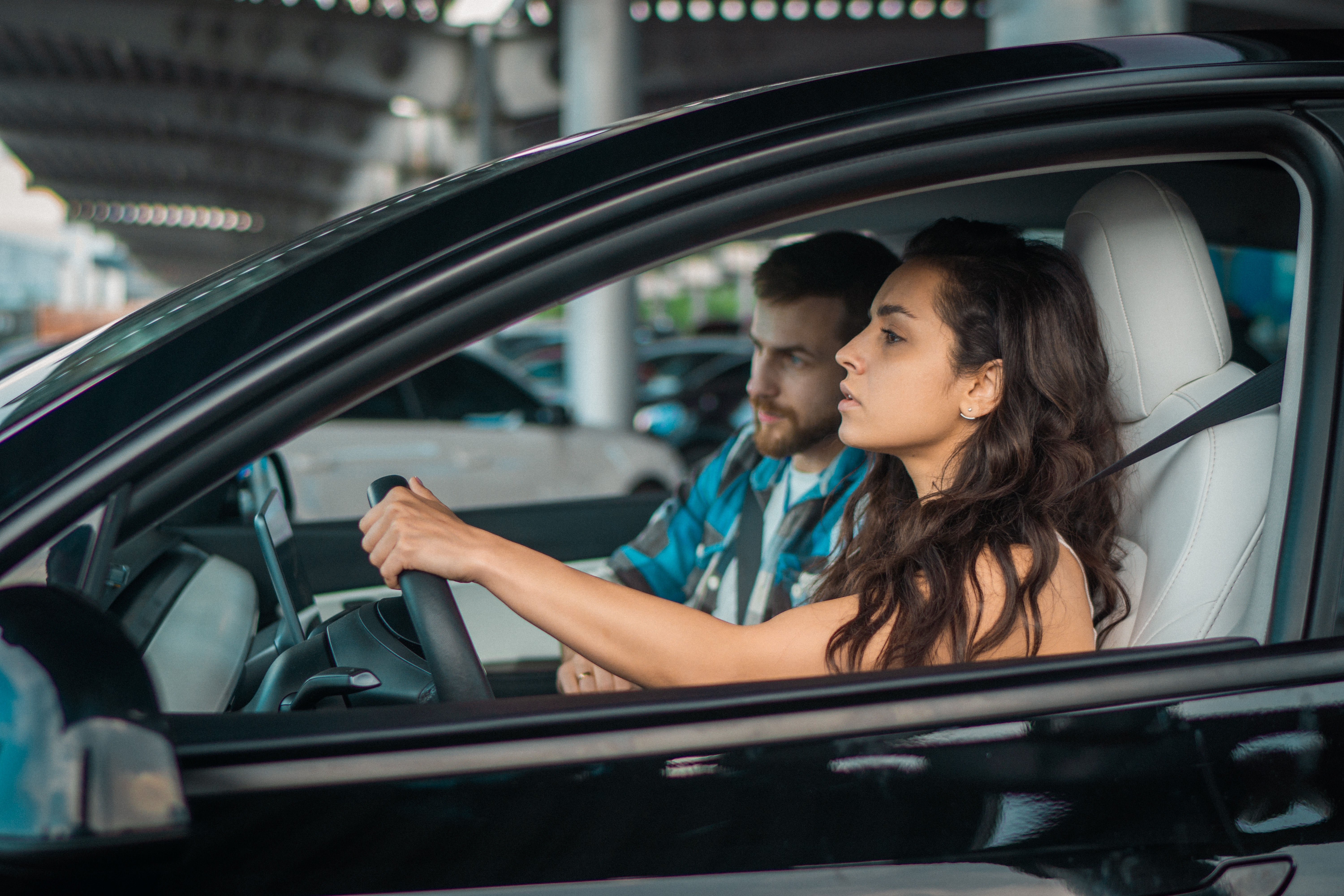 Young woman looking at the road while driving instructor sitting on the passenger seat during drive test. Driving test, driver courses, exam concept | Source: Shutterstock