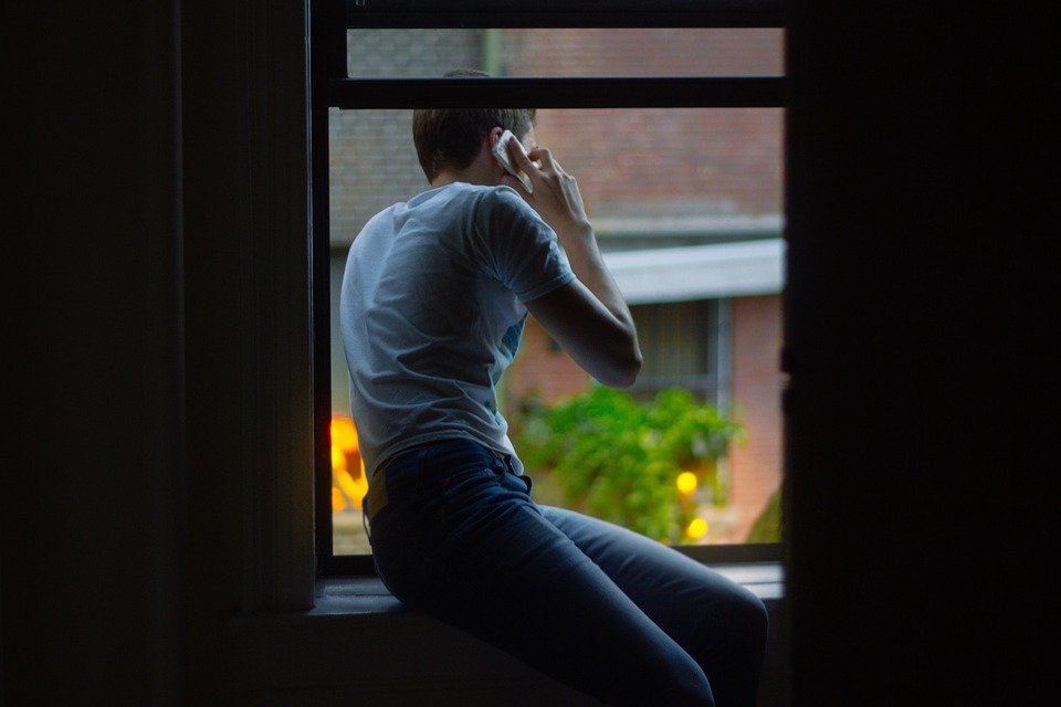 Hombre asomado por una ventana mientras habla por teléfono. | Foto: Pixabay