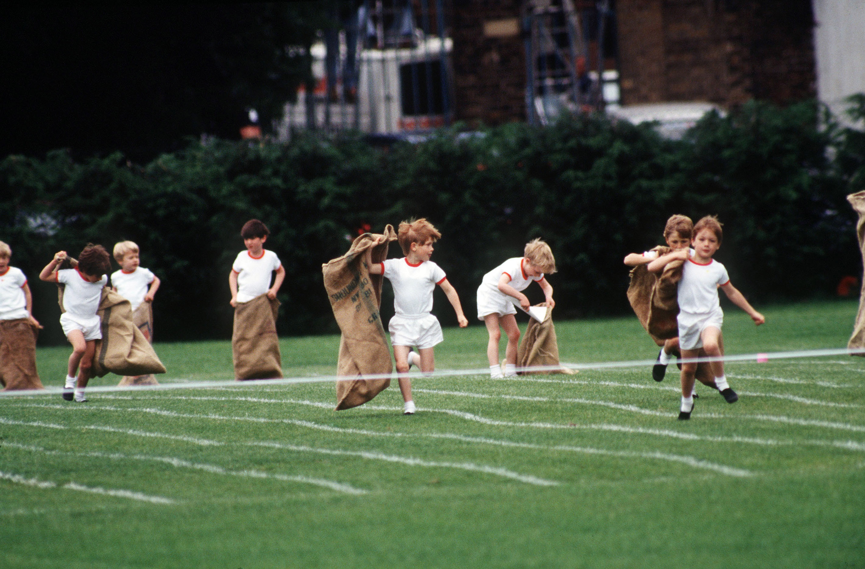 A young Prince Harry gave it his all during the sack race, gripping the coarse hessian tightly as he launched into the air with wide-eyed determination. With classmates leaping and stumbling around him, the moment captured the innocent energy of childhood competition.