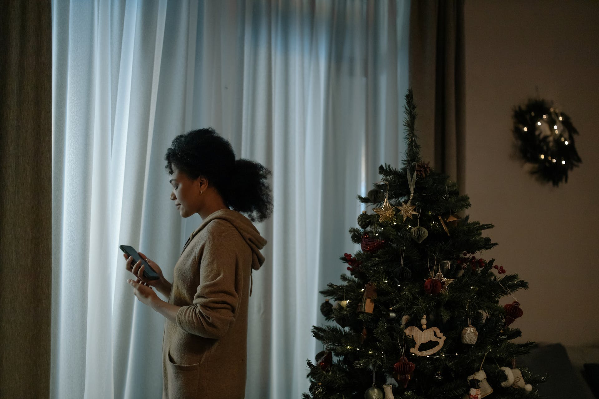 Woman with a phone standing beside a Christmas tree | Source: Pexels