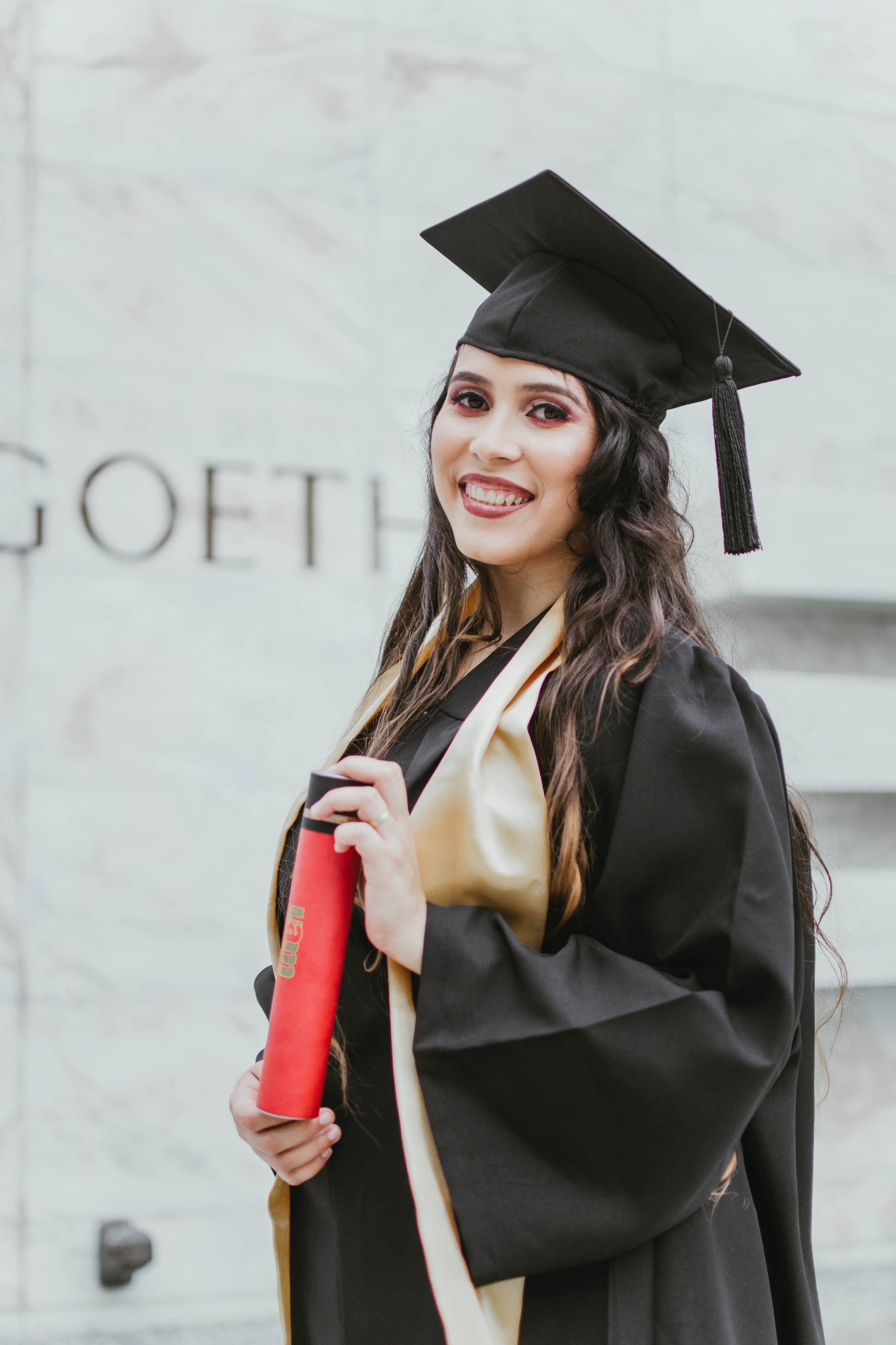 A young woman dressed in academic attire while holding a qualification | Source: Pexels