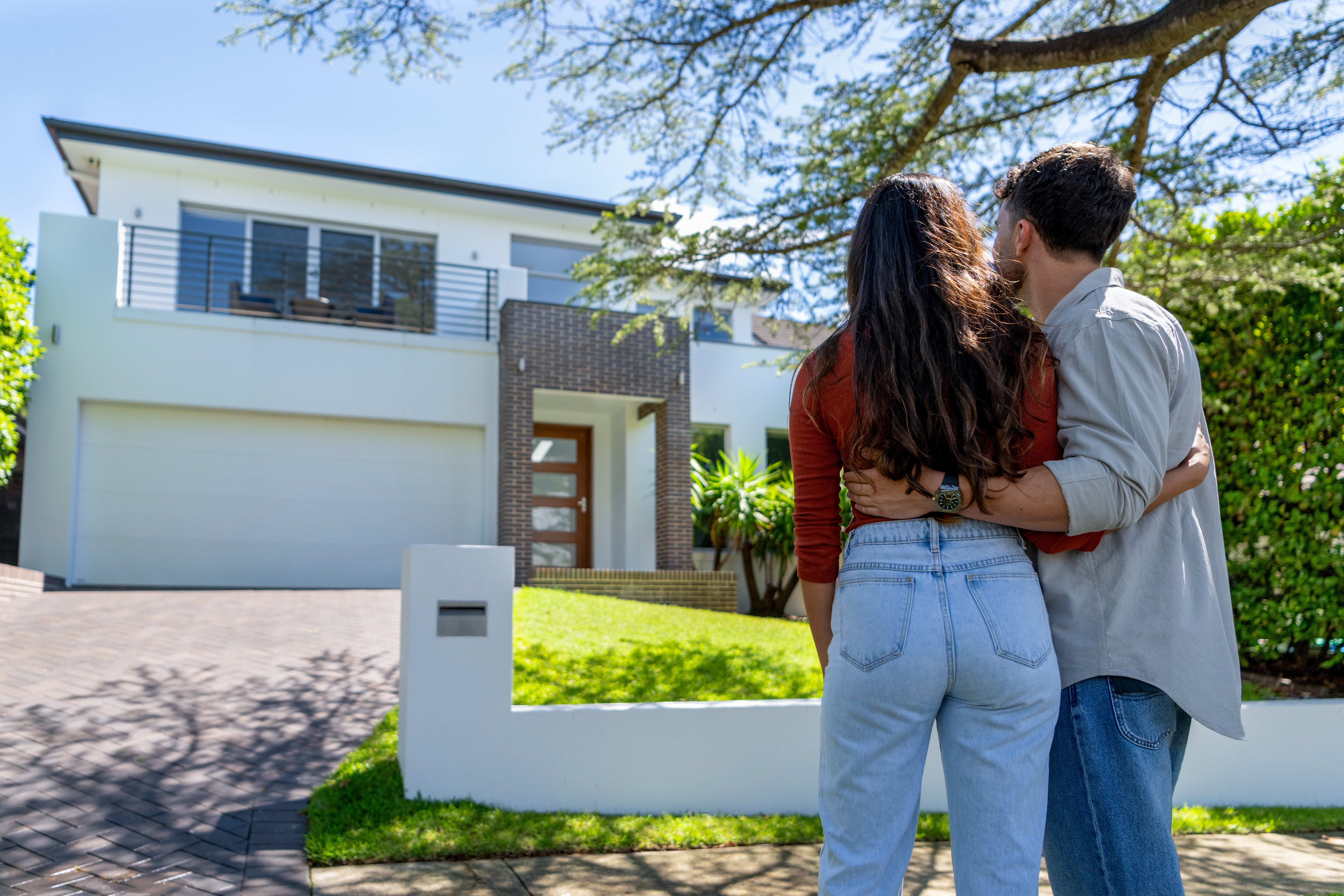 Happy Couple standing in front of their new home. They are both wearing casual clothes and embracing. Rear view | Source: Getty Images