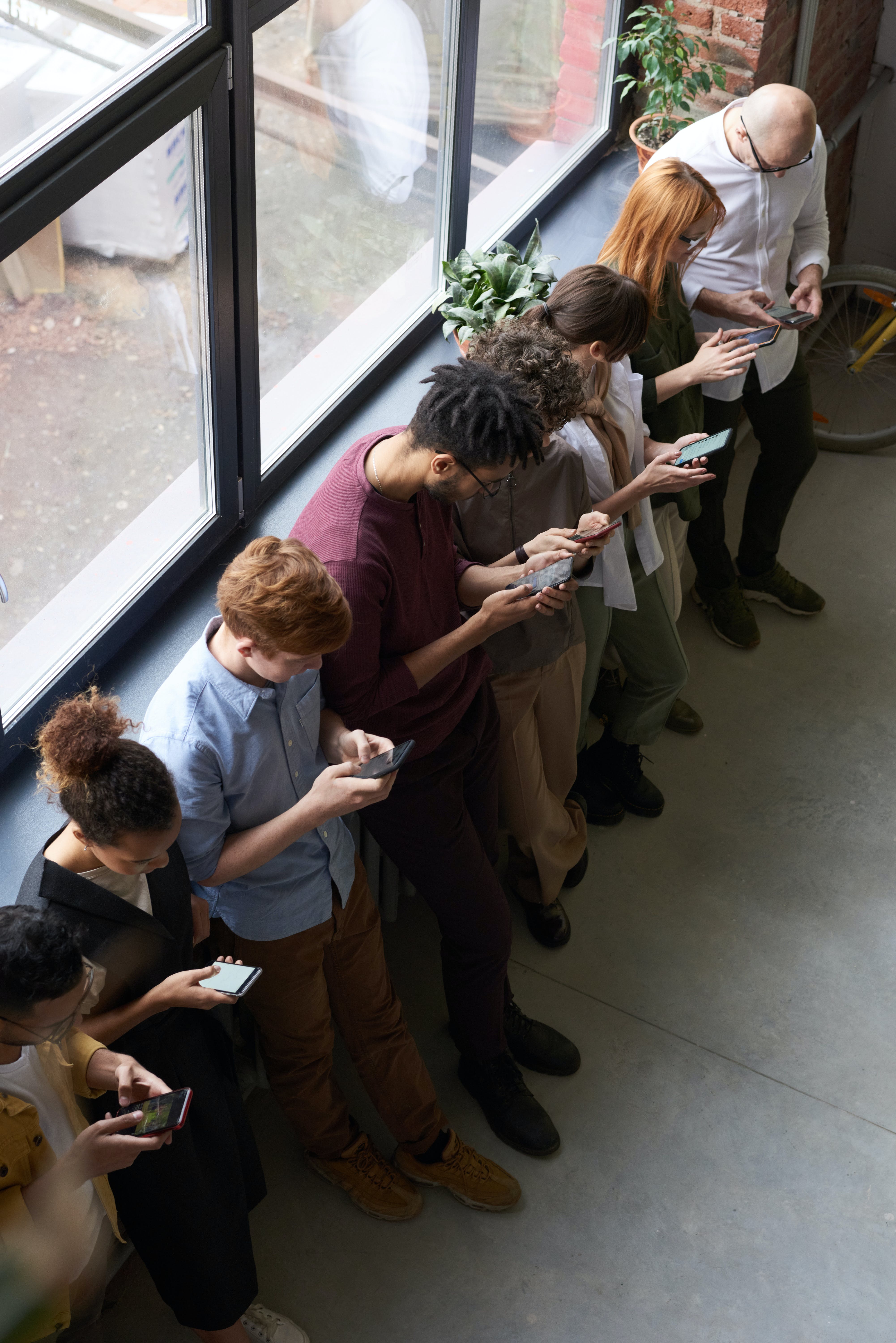 People standing in a queue while operating their smartphones. | Source: Pexels