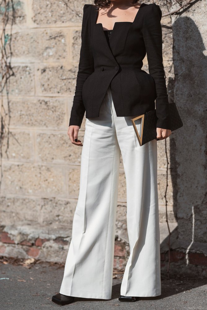 Mujer usando un blazer corto de tela oscura ajustado en la cintura y un pantalón color hueso. | Foto: Shutterstock