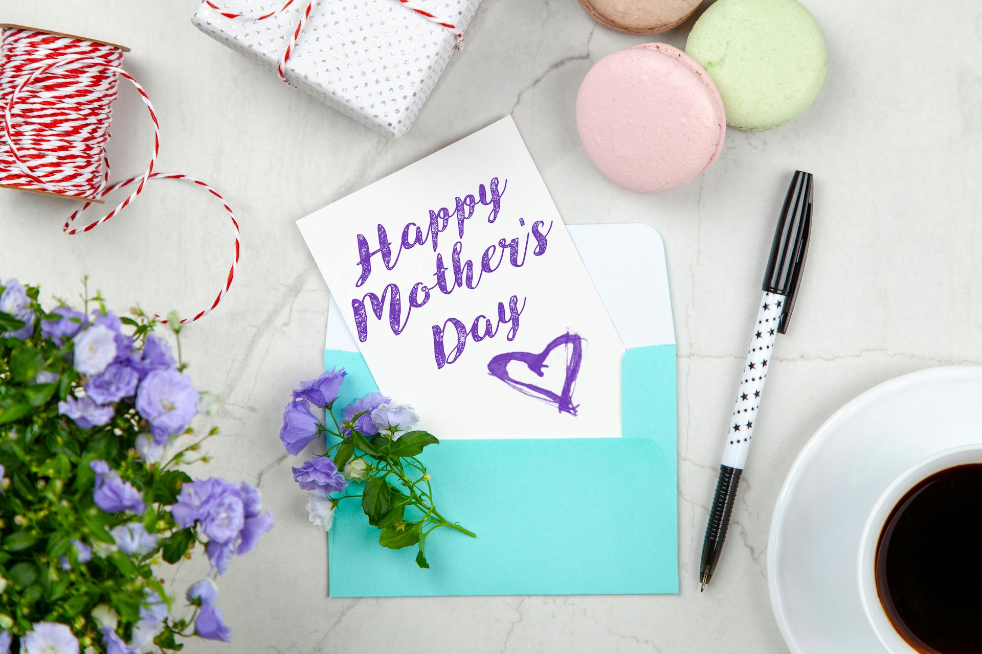 A Mother's Day card lying beside a pen, macaroons, flowers, and a box near a coffee cup | Source: Pexels