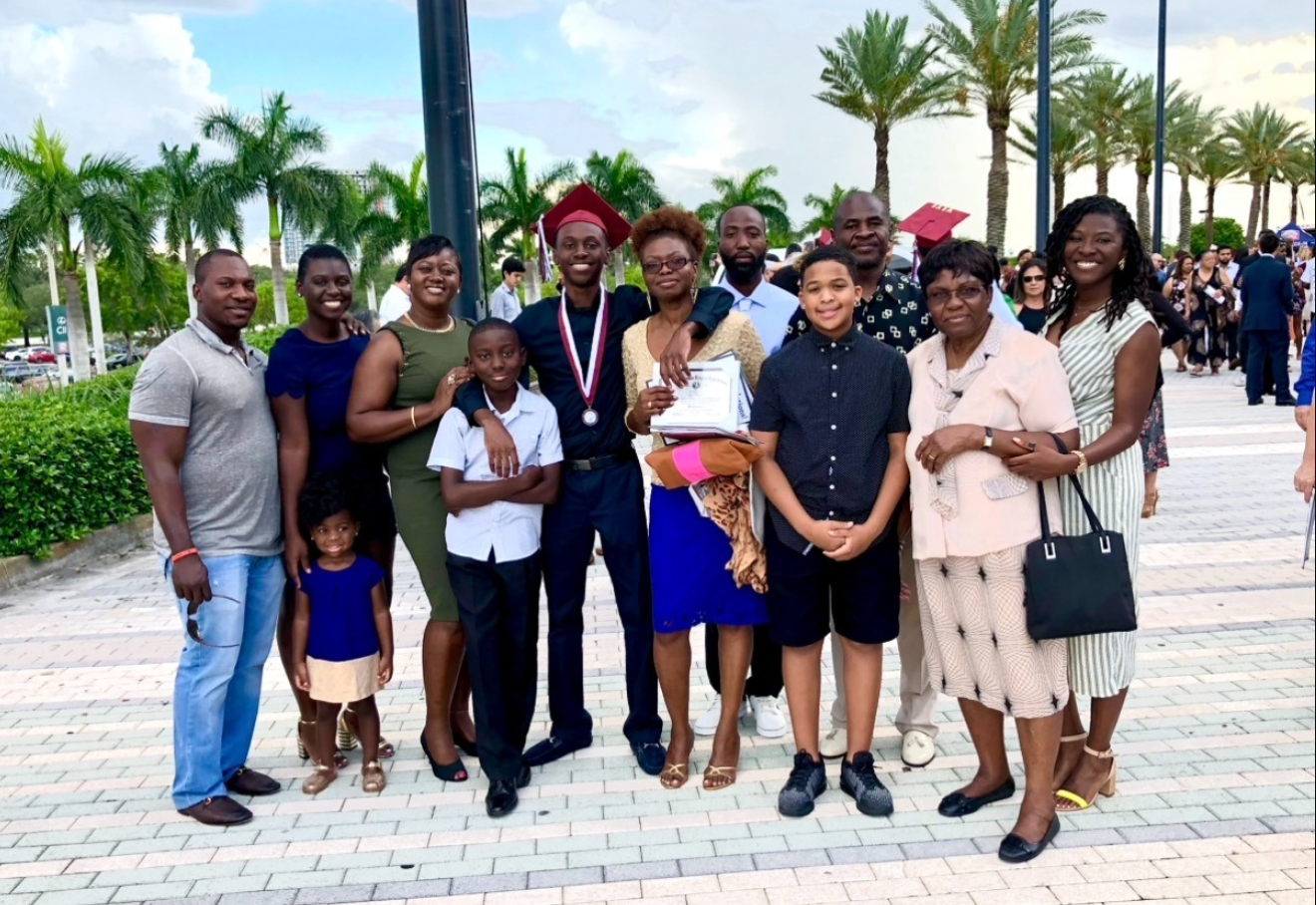 Surrounded by loved ones at a graduation celebration, Nancy Metayer Bowen stands proudly with her brother—dressed in cap and medal—while family members gather closely around, capturing a joyful moment of achievement and togetherness. | Source: Gofundme