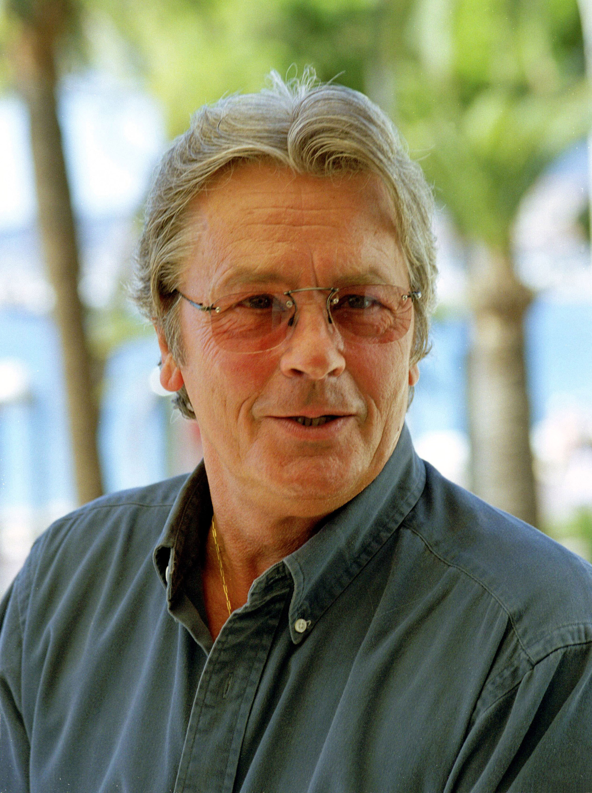 Delon, who was 61 in 2000, still carried the mystique that made him an icon of European cinema. In a relaxed moment, he wore tinted glasses and an open-collar shirt, his tousled silver hair and quiet confidence lending him the look of a man who had nothing to prove. The image captured an aging legend, unfussy and effortlessly charismatic.