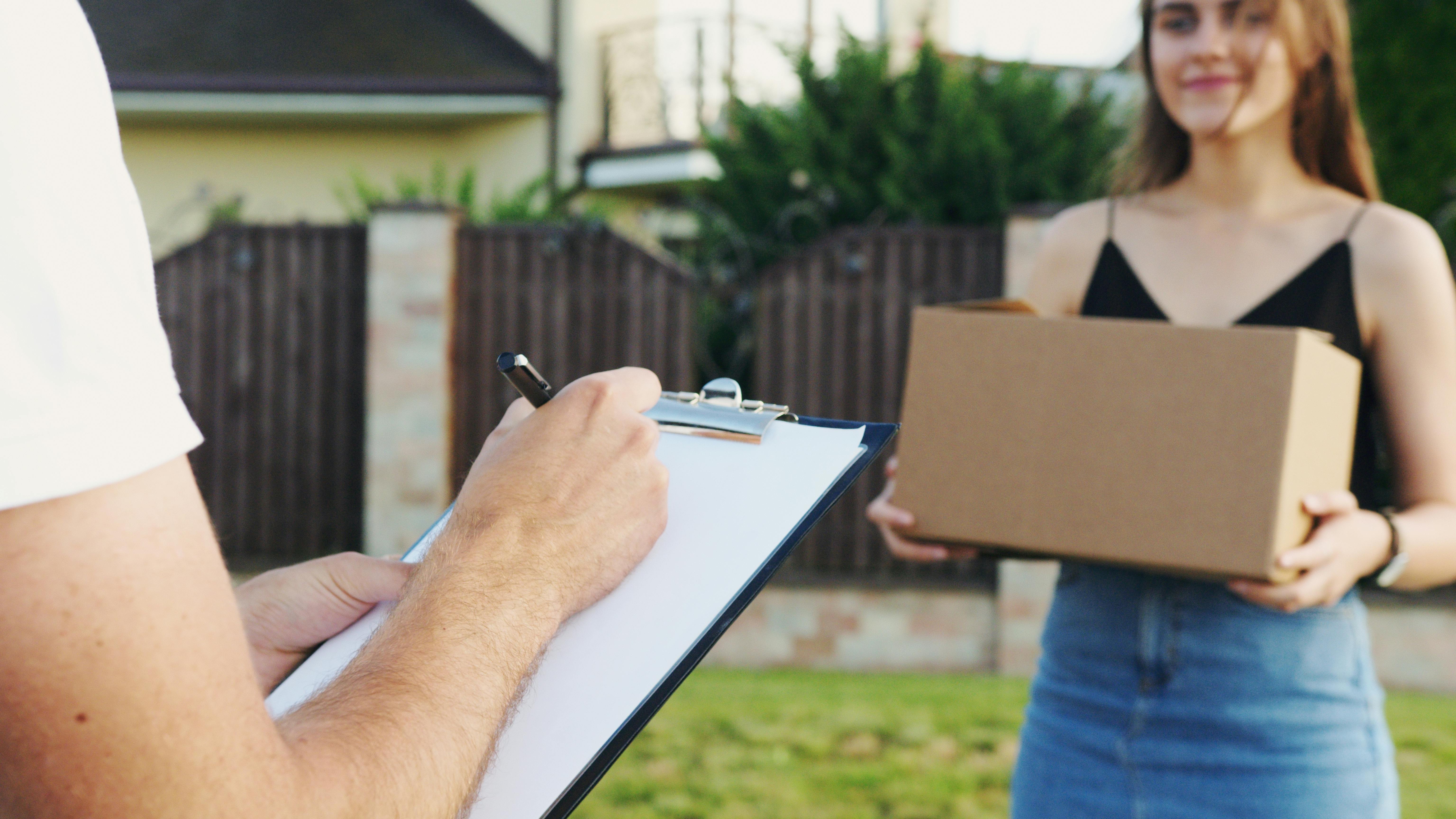 A woman holding a box with a man writing something down | Source: Pexels