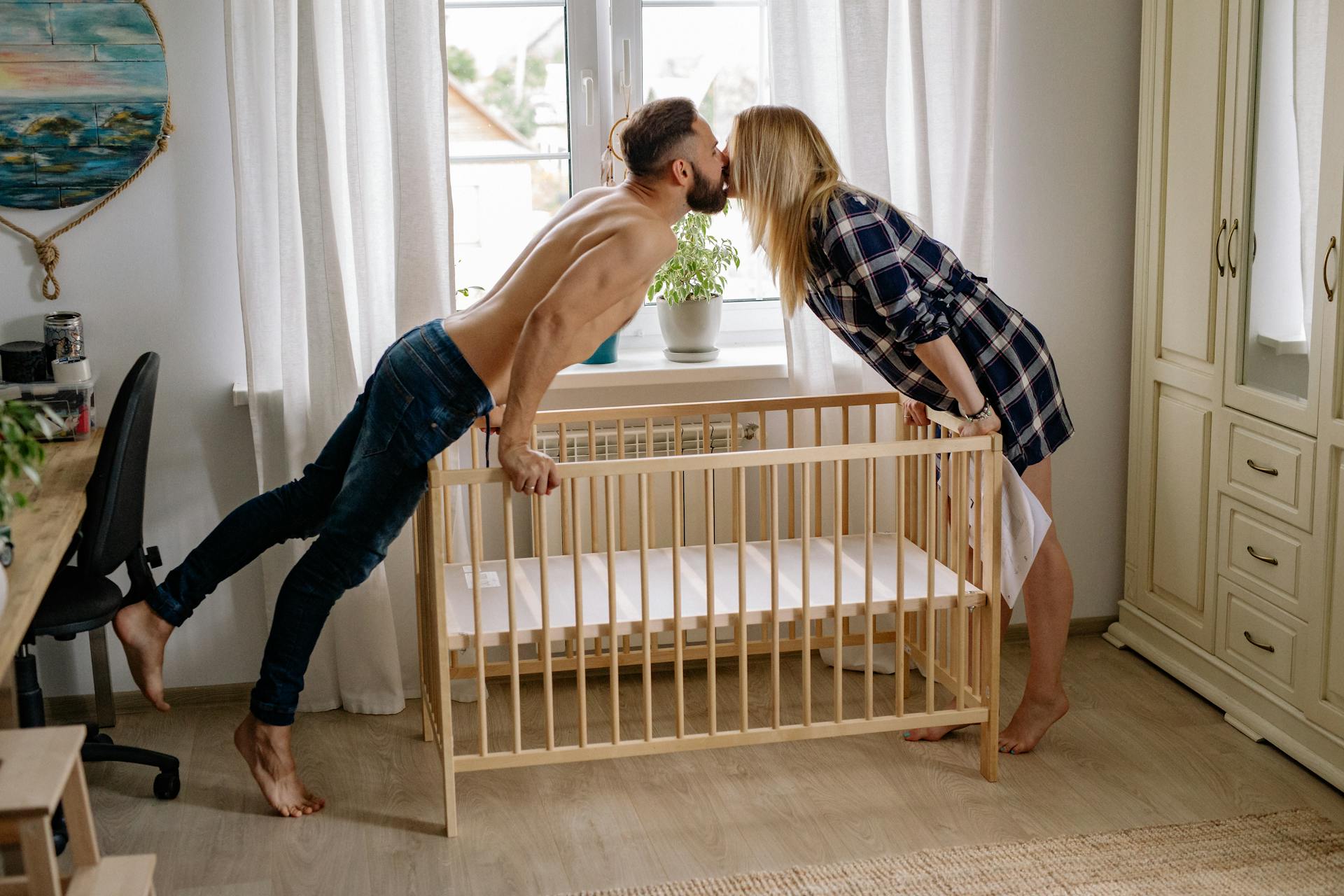A couple kissing while setting up a baby crib | Source: Pexels