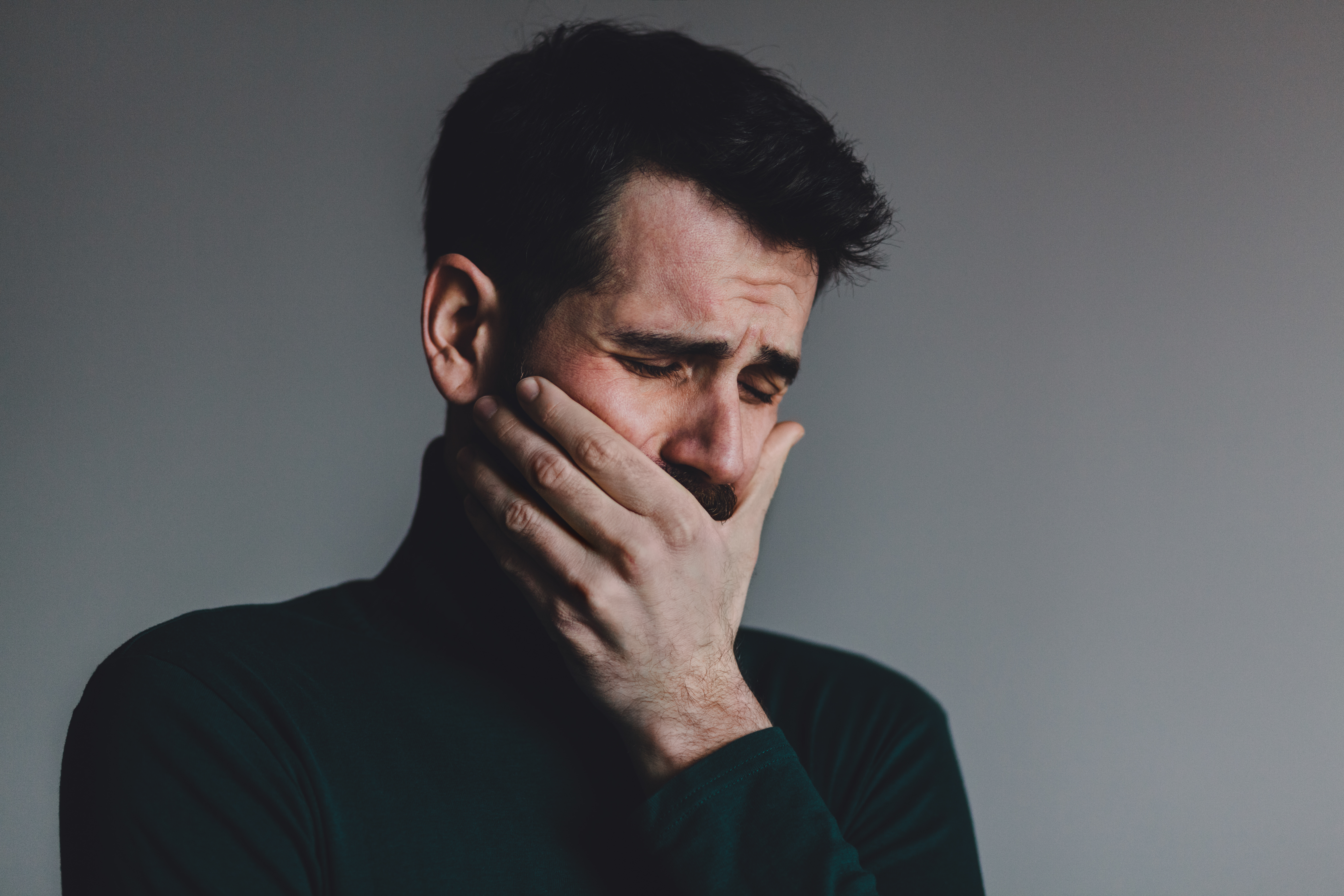 A man holding his mouth as he cries | Source: Shutterstock