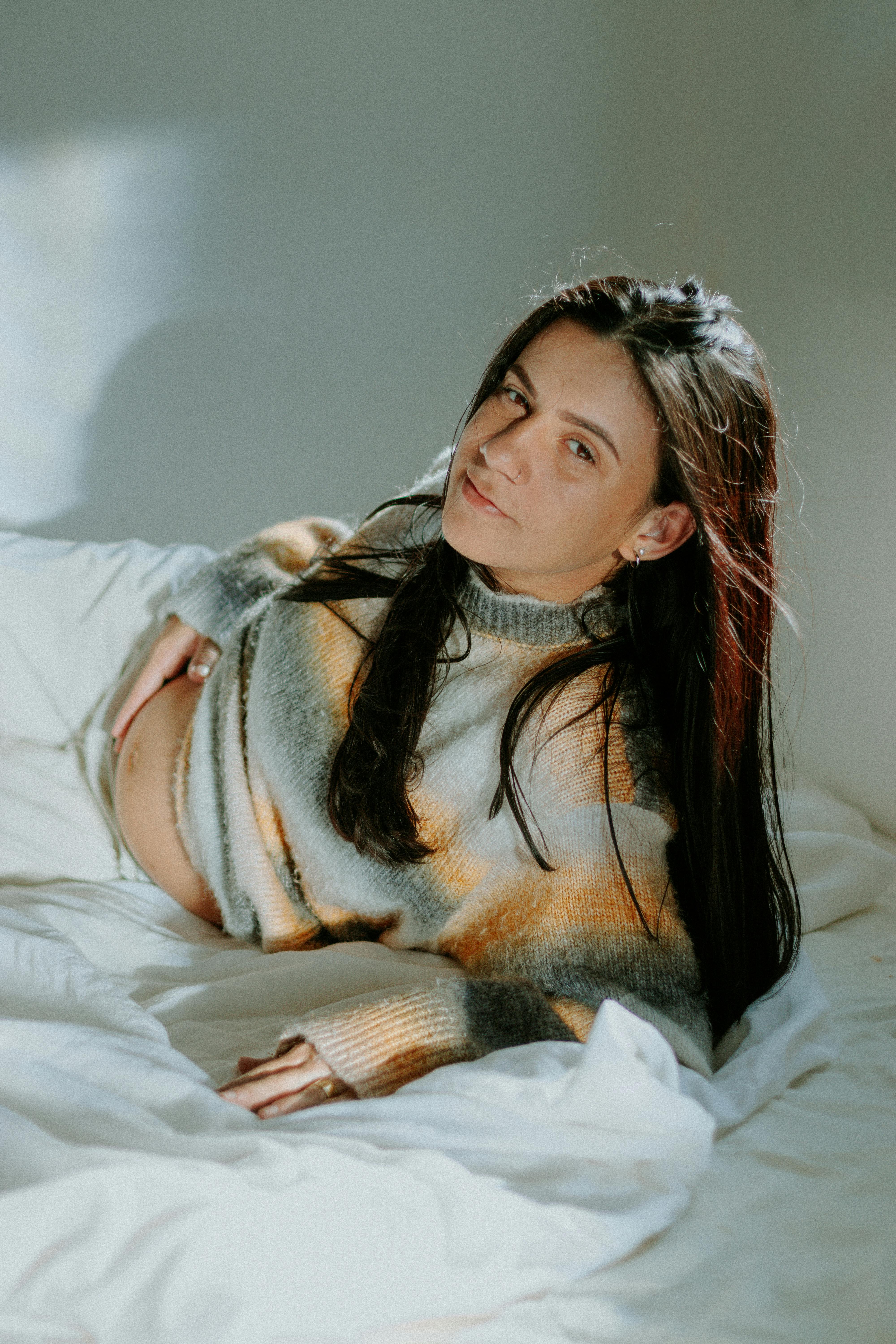 A pregnant woman looking displeased while lying on a bed | Source: Pexels