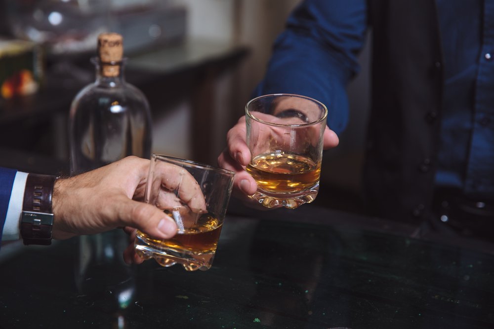A close-up of two men clinking glasses of whiskey while at bar counter in a pub | Photo: Shutterstock/Romanno