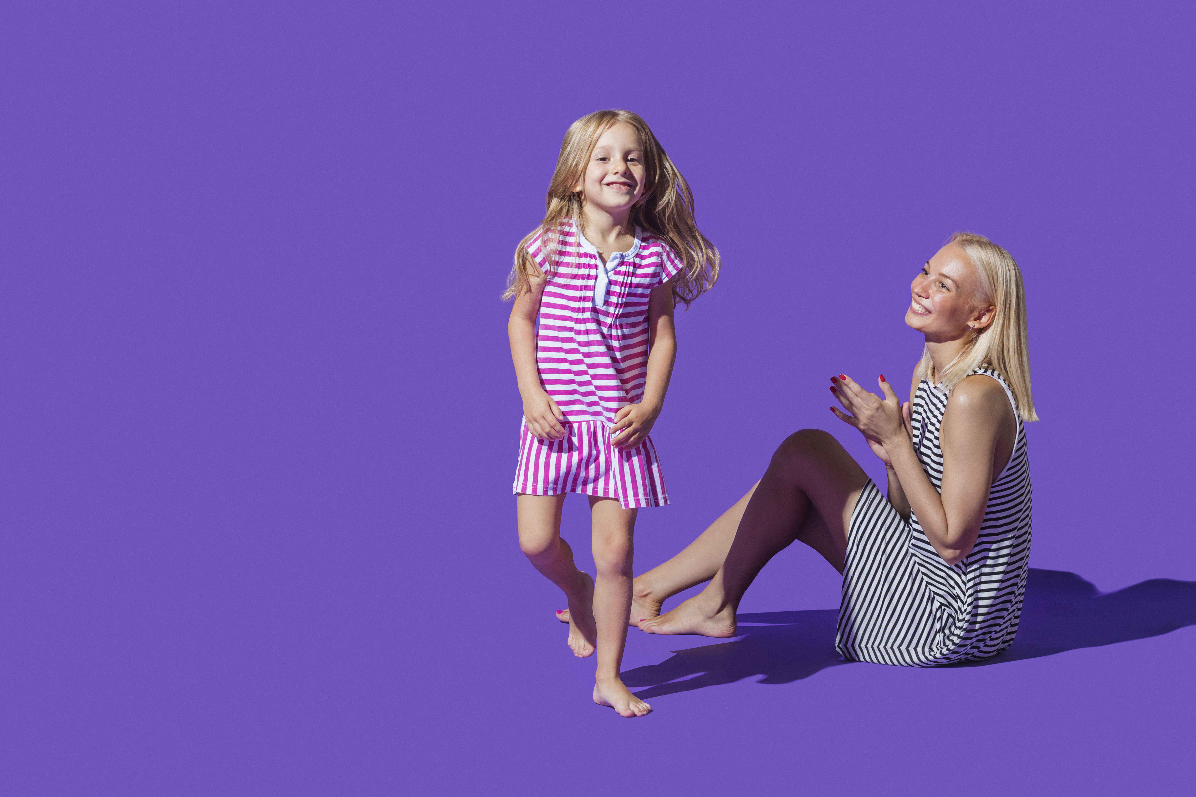 Portrait playful mother and daughter in striped dresses against purple background | Source: Getty Images