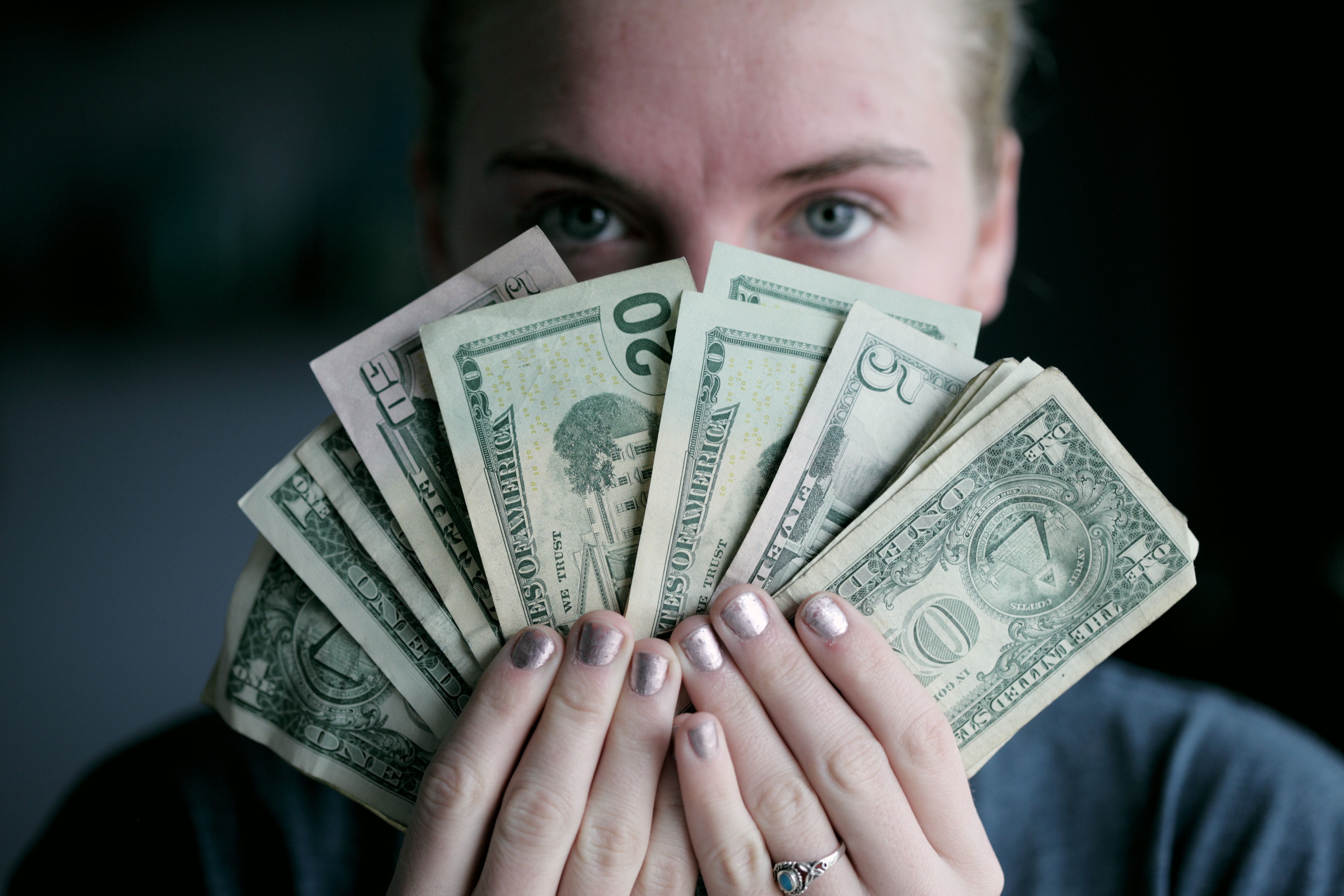 An individual holding money in front of their face. │Source: Unsplash