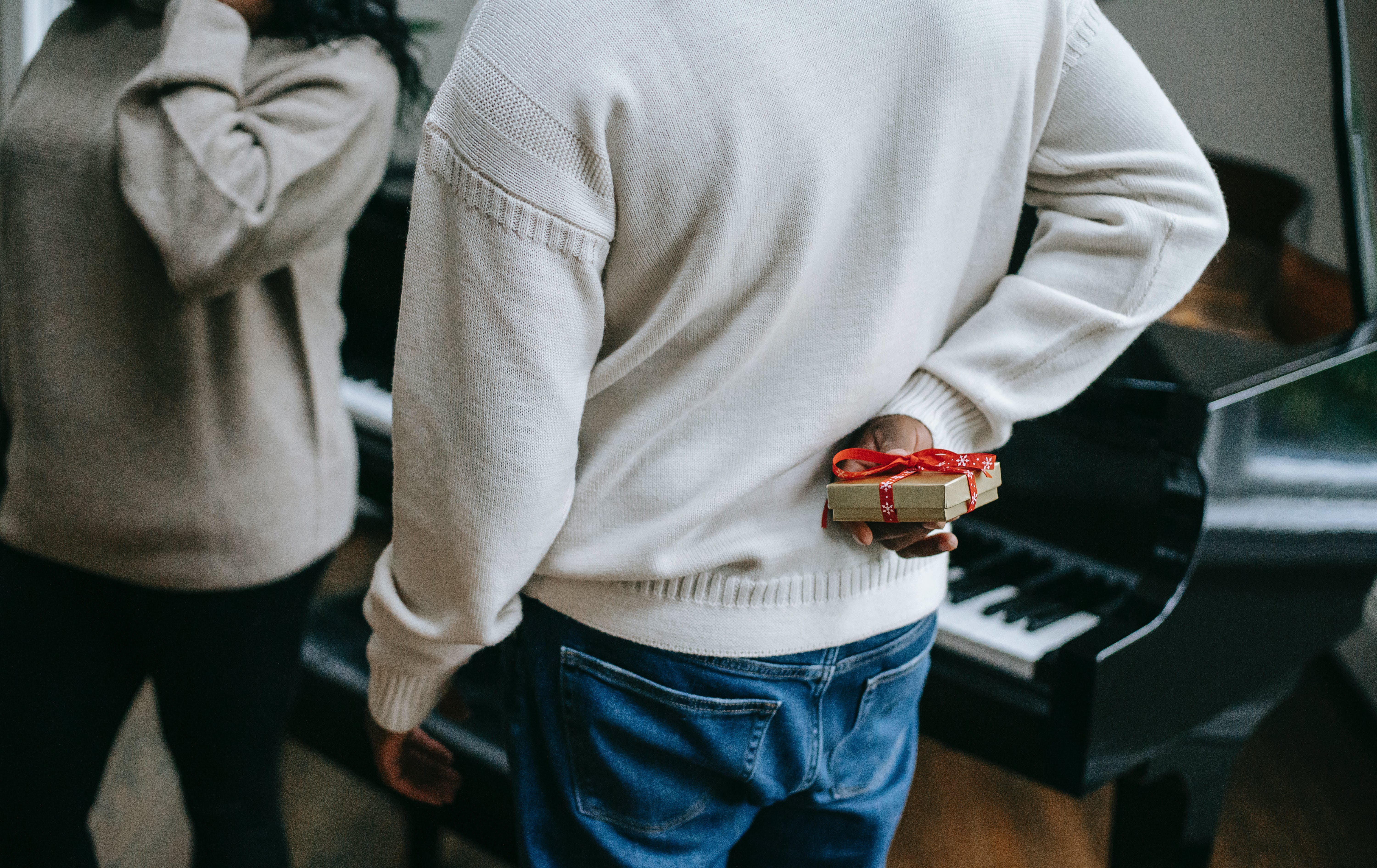 A man hiding a Christmas gift behind his back from his partner | Source: Pexels