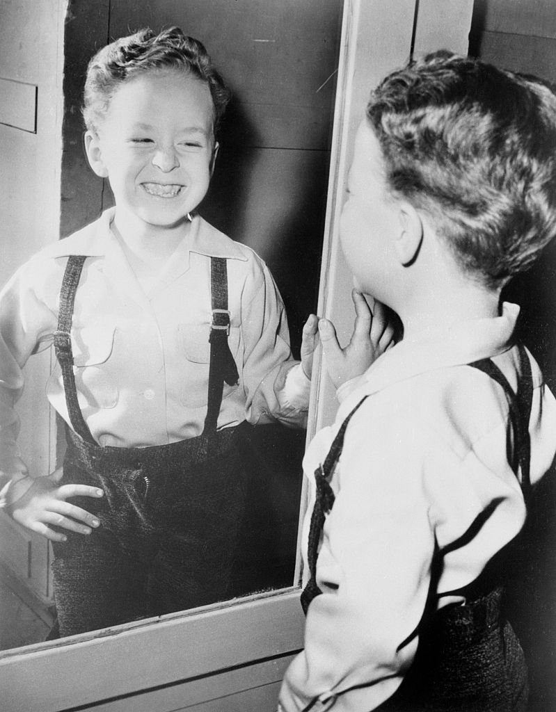 A portrait of Rusty Hamer looking and smiling at his image in a mirror on January 01, 1955 | Photo: Getty Images