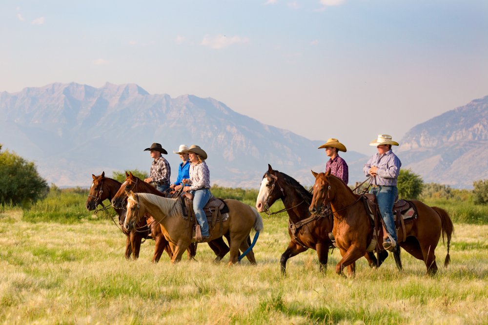 A group of friends horseback riding in the grassy fields with the mountains in the background. | Photo: Shutterstock.