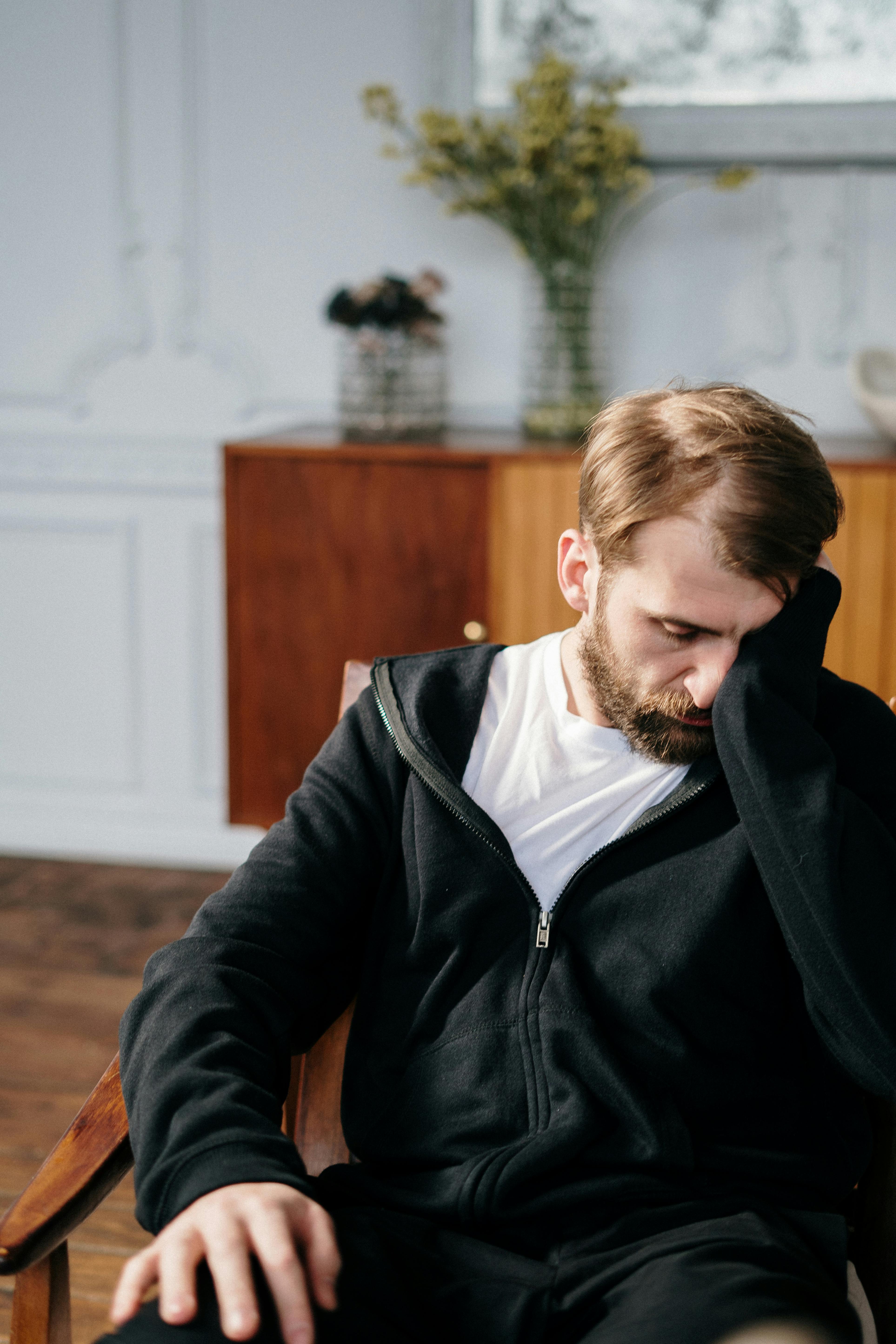 An ashamed and sad man sitting on a chair covering part of his face with his hand | Source: Pexels