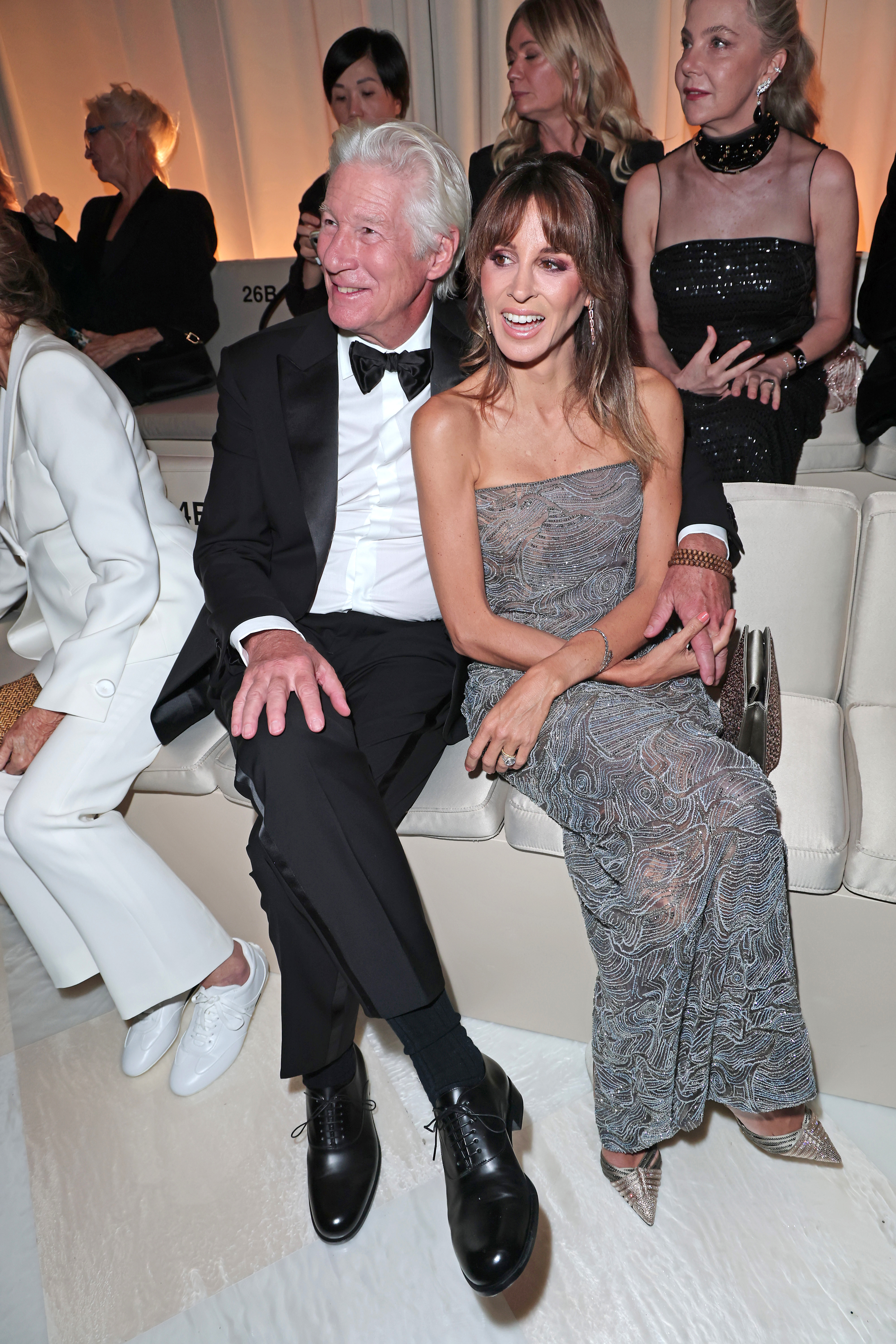Alejandra Silva beams with laughter as Richard Gere looks on with a subtle smile, their front-row presence capturing a light moment amid the high-fashion intensity.