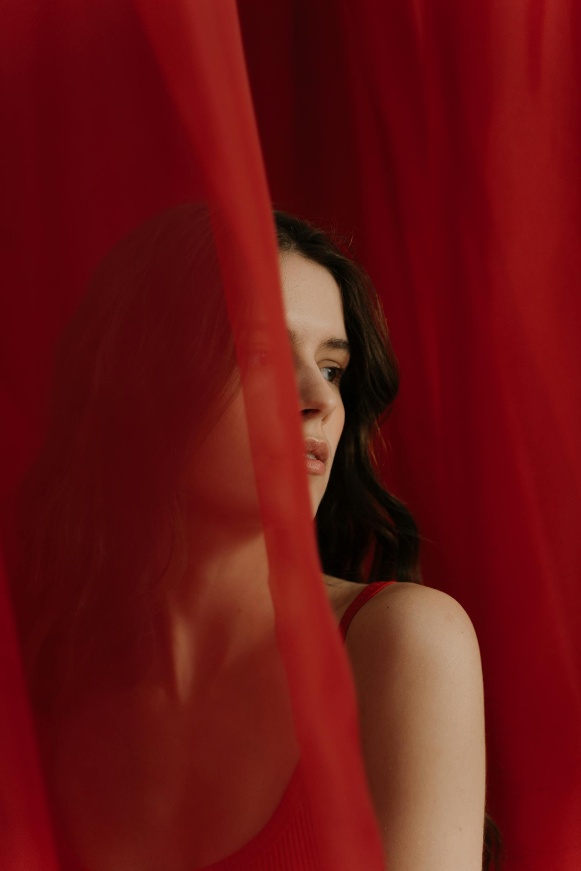 A woman in a red dress standing behind a curtain | Source: Pexels