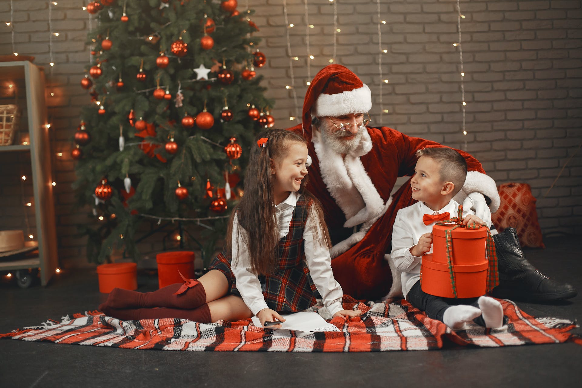 Man in Santa Claus costume sitting with a boy and a girl beside a Christmas tree | Source: Pexels