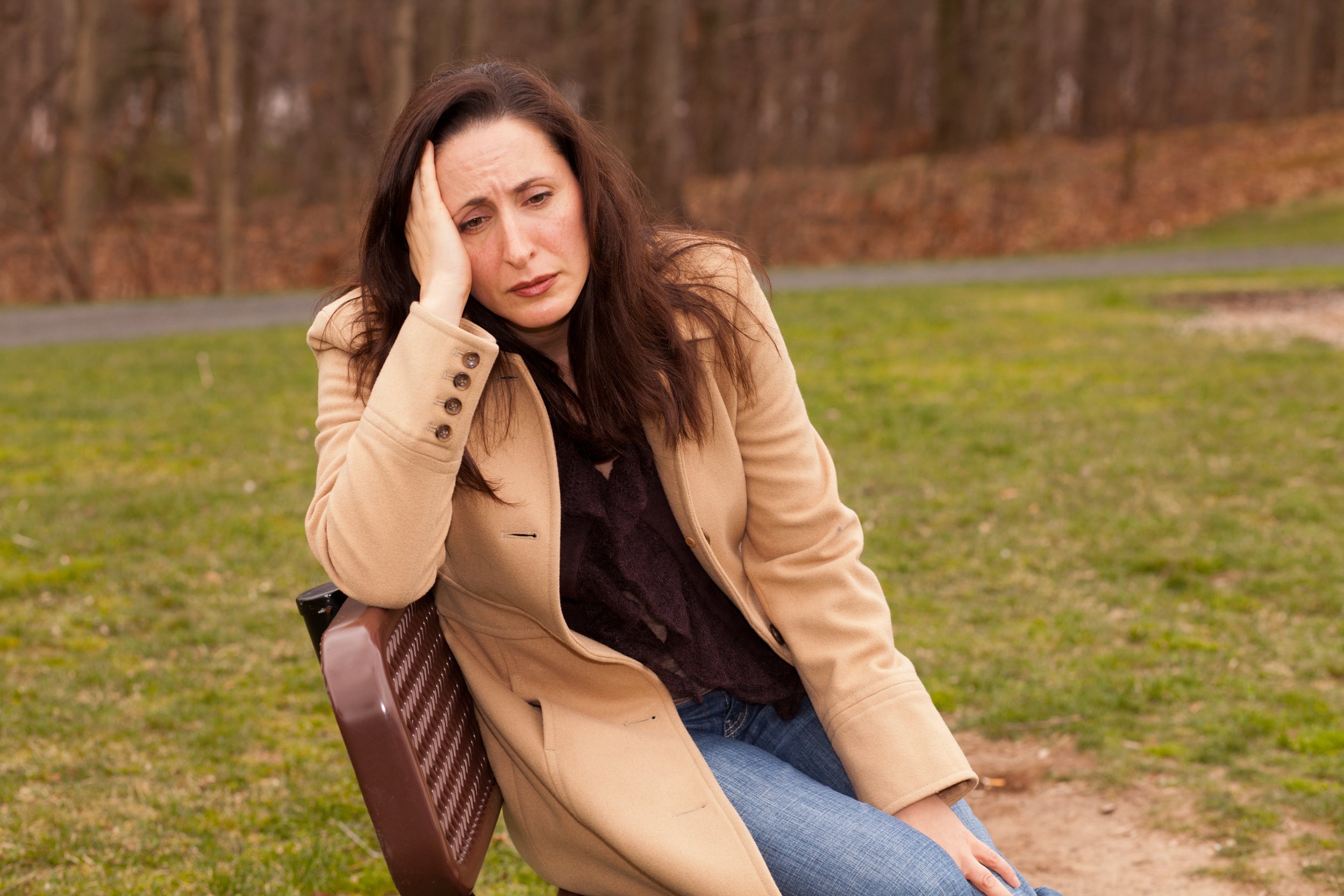 Traurige Frau sitzt auf einer Bank in einem Mantel und sieht einsam aus | Quelle: Shutterstock