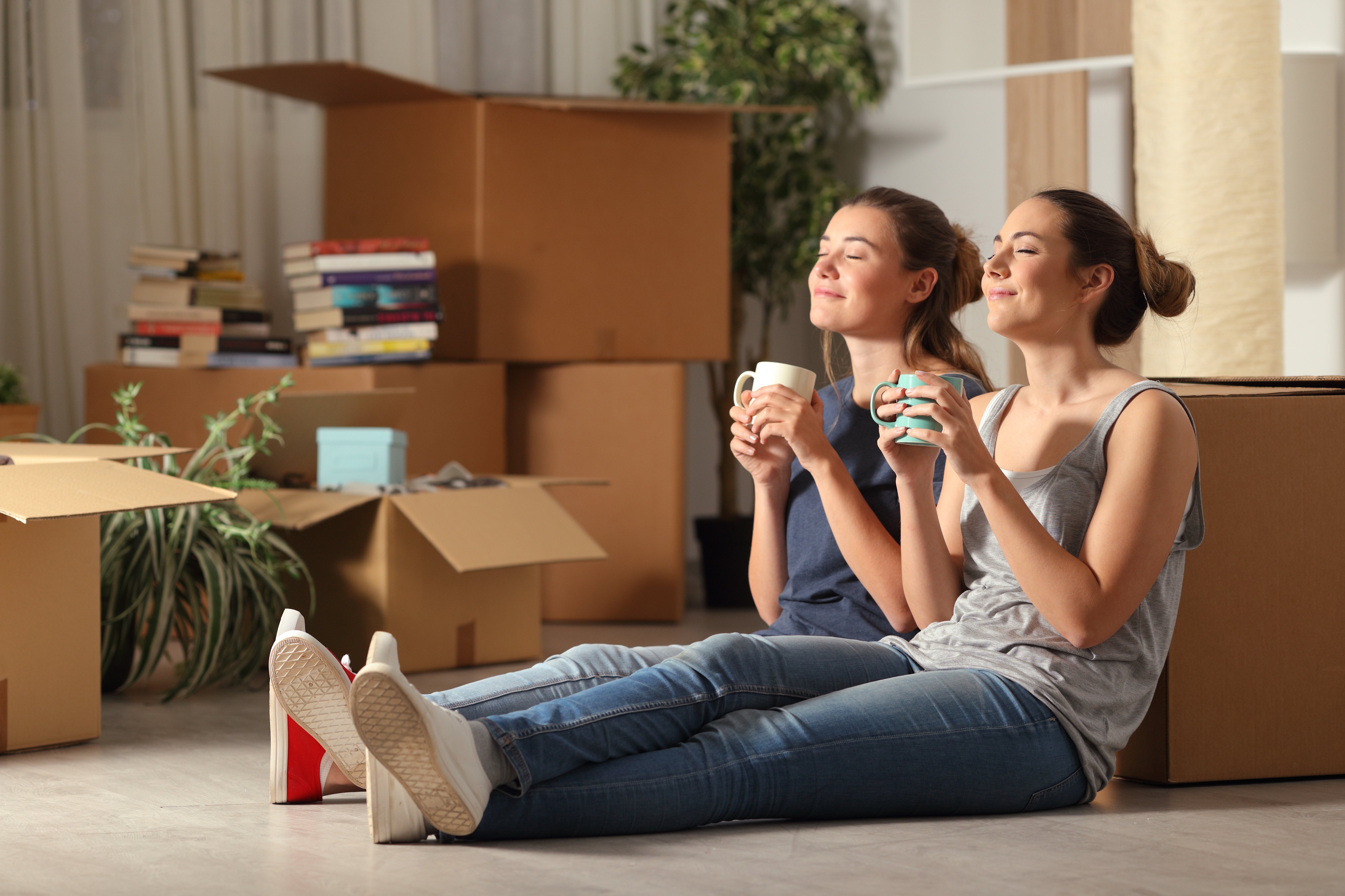 Two young women happily holding mugs while resting from unpacking. | Source: Shutterstock