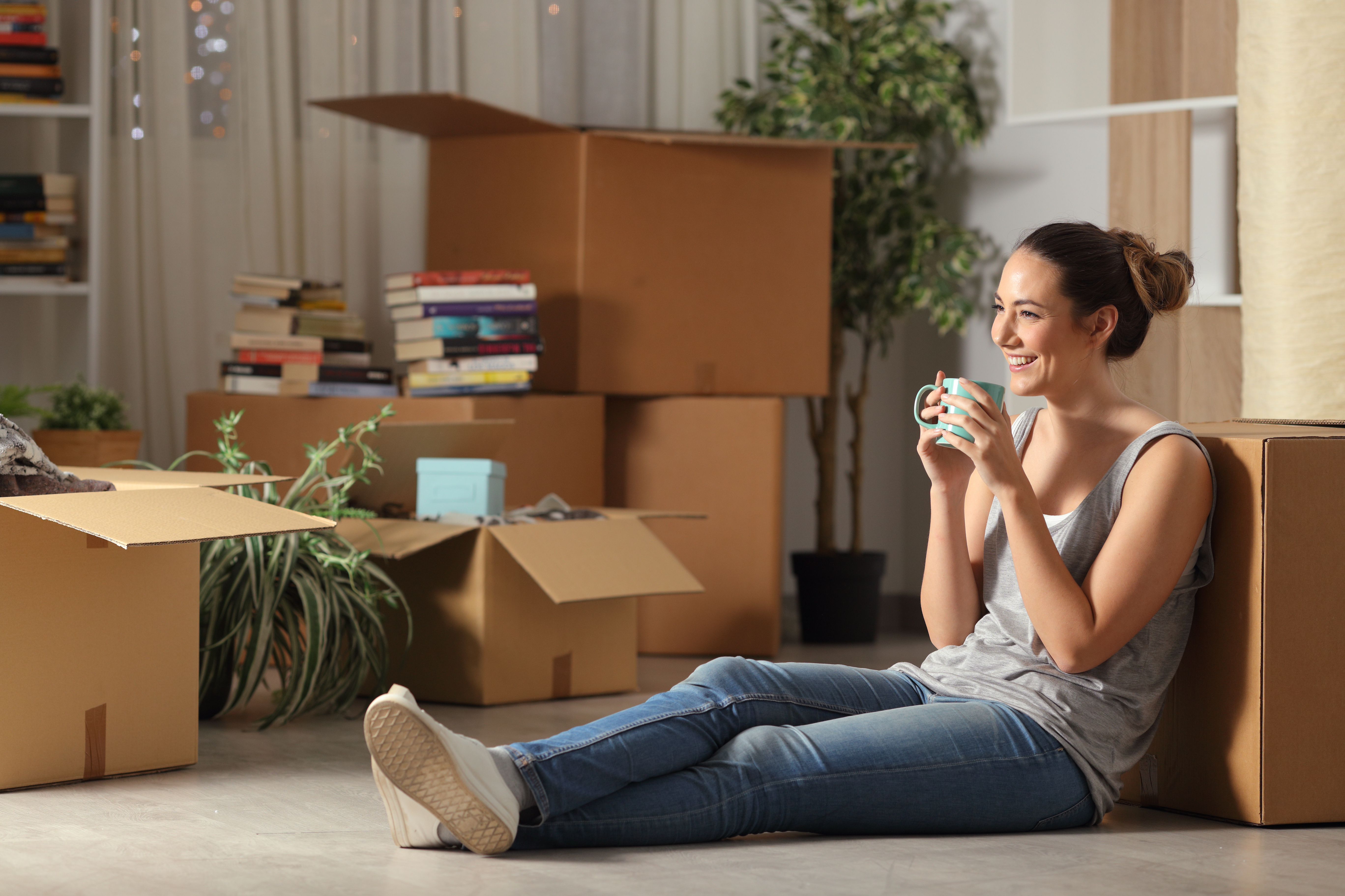 A young girl sitting on the floor, surrounded by moving boxes, drinking coffee | Source: Shutterstock