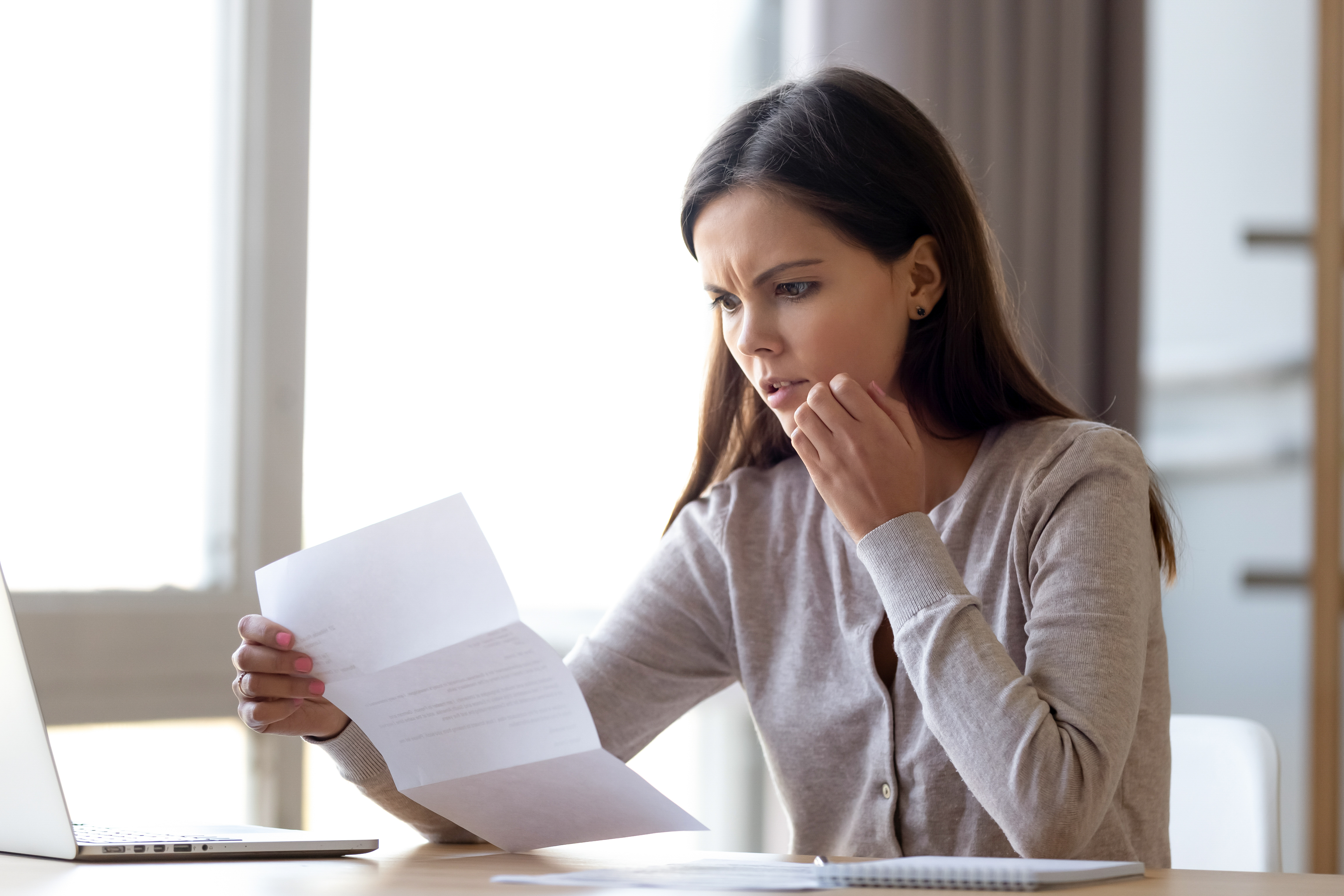 A young woman looking confused as she stares at a piece of paper | Source: Shutterstock