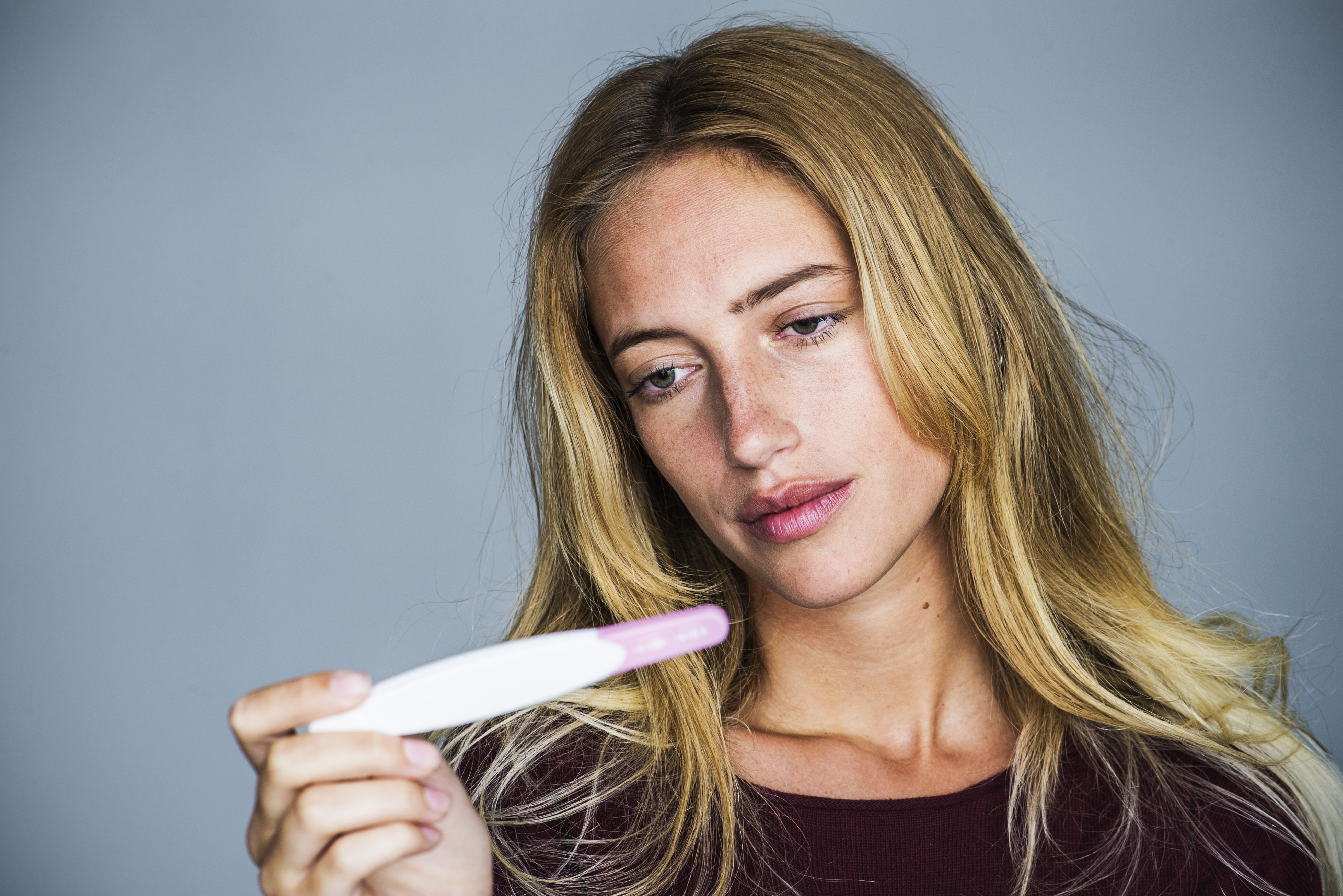 Young woman looking at pregnancy test with disappointed expression | Source: Getty Images
