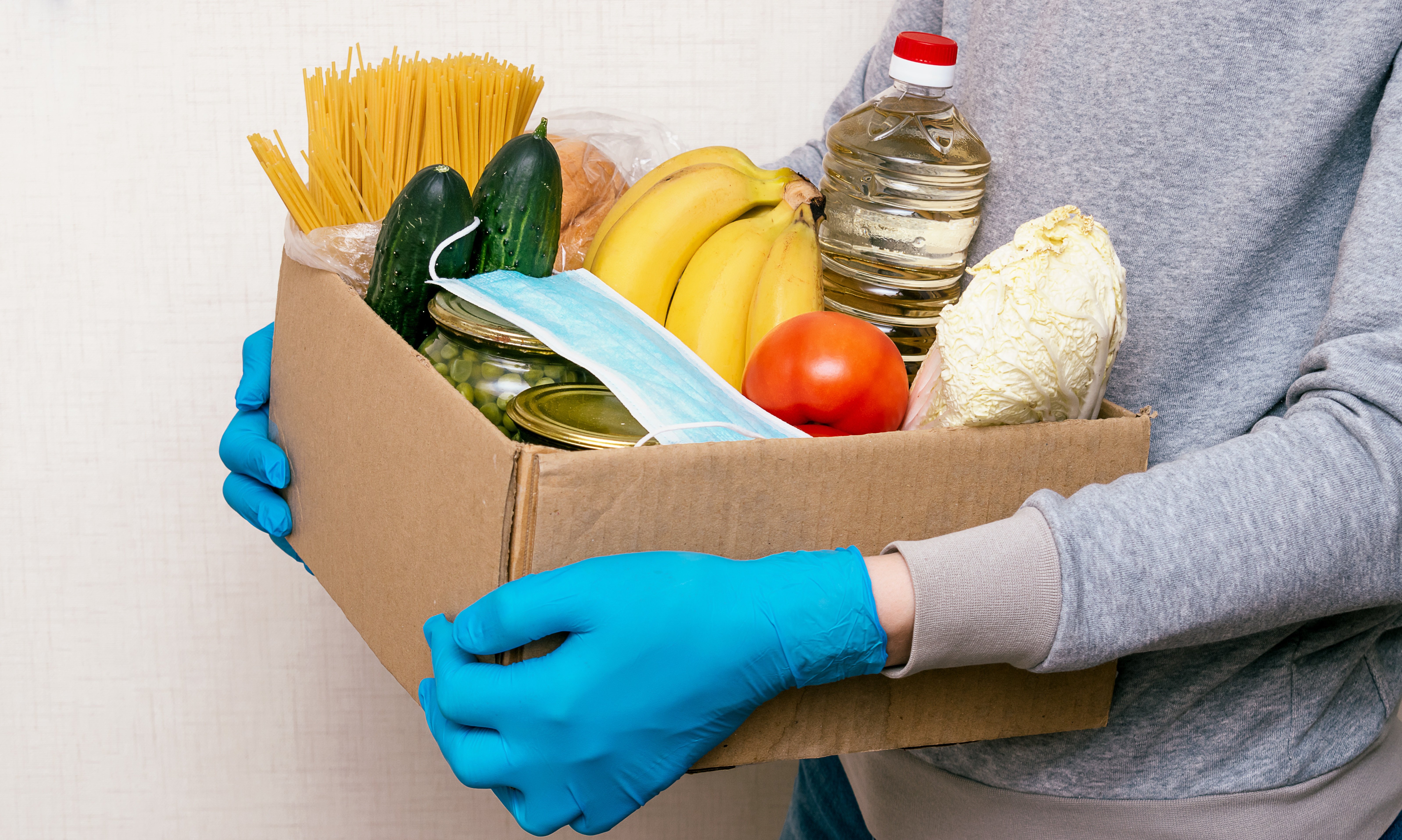 Mujer con guantes de goma sosteniendo una caja de alimentos entre sus brazos. | Foto: Shutterstock
