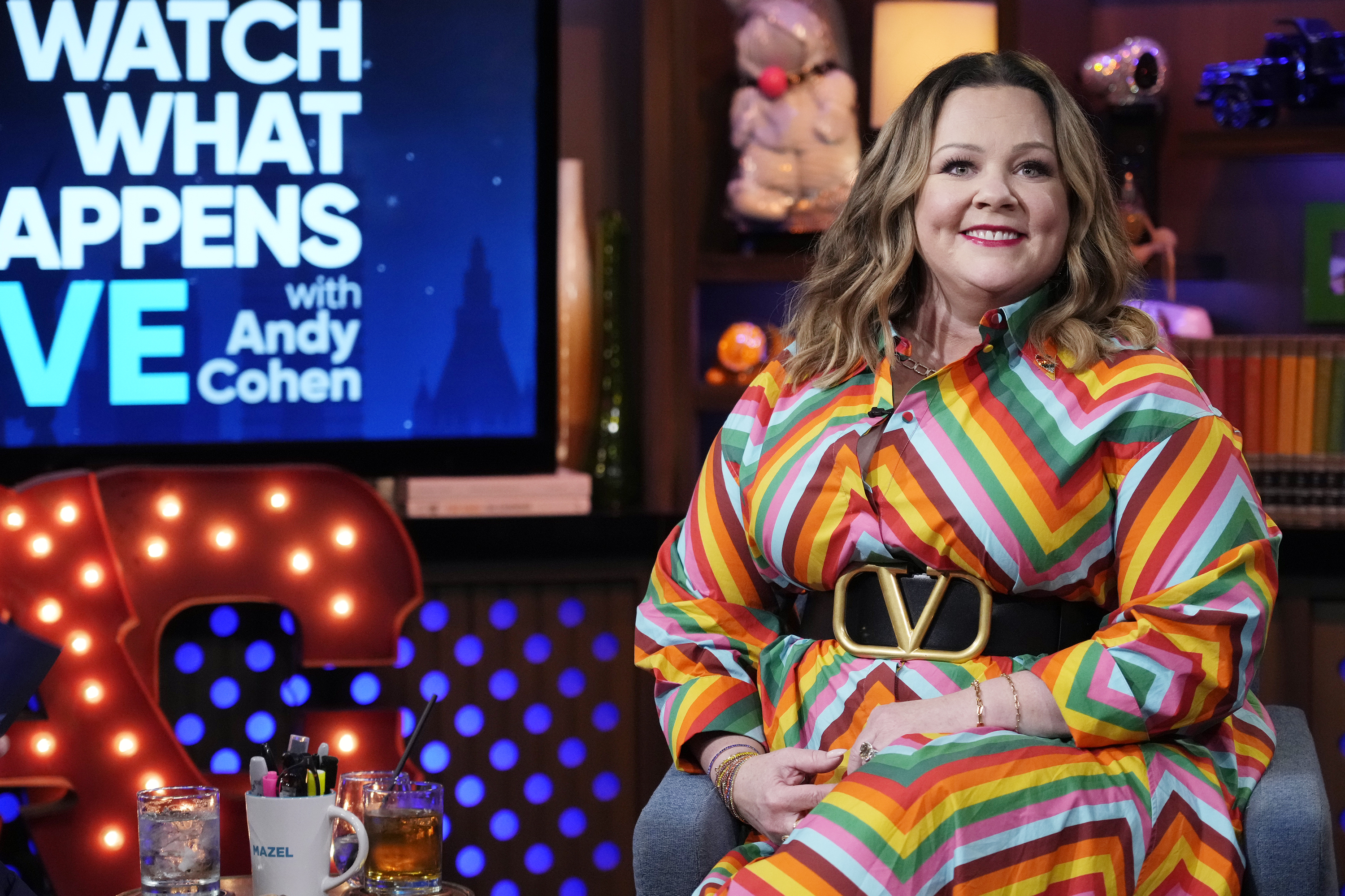 Melissa McCarthy brightens the studio in a bold rainbow-striped dress cinched with a statement belt, matching the "Watch What Happens Live With Andy Cohen" show's lively energy. With an easy smile and relaxed posture, she adds a joyful spark to the late-night conversation.