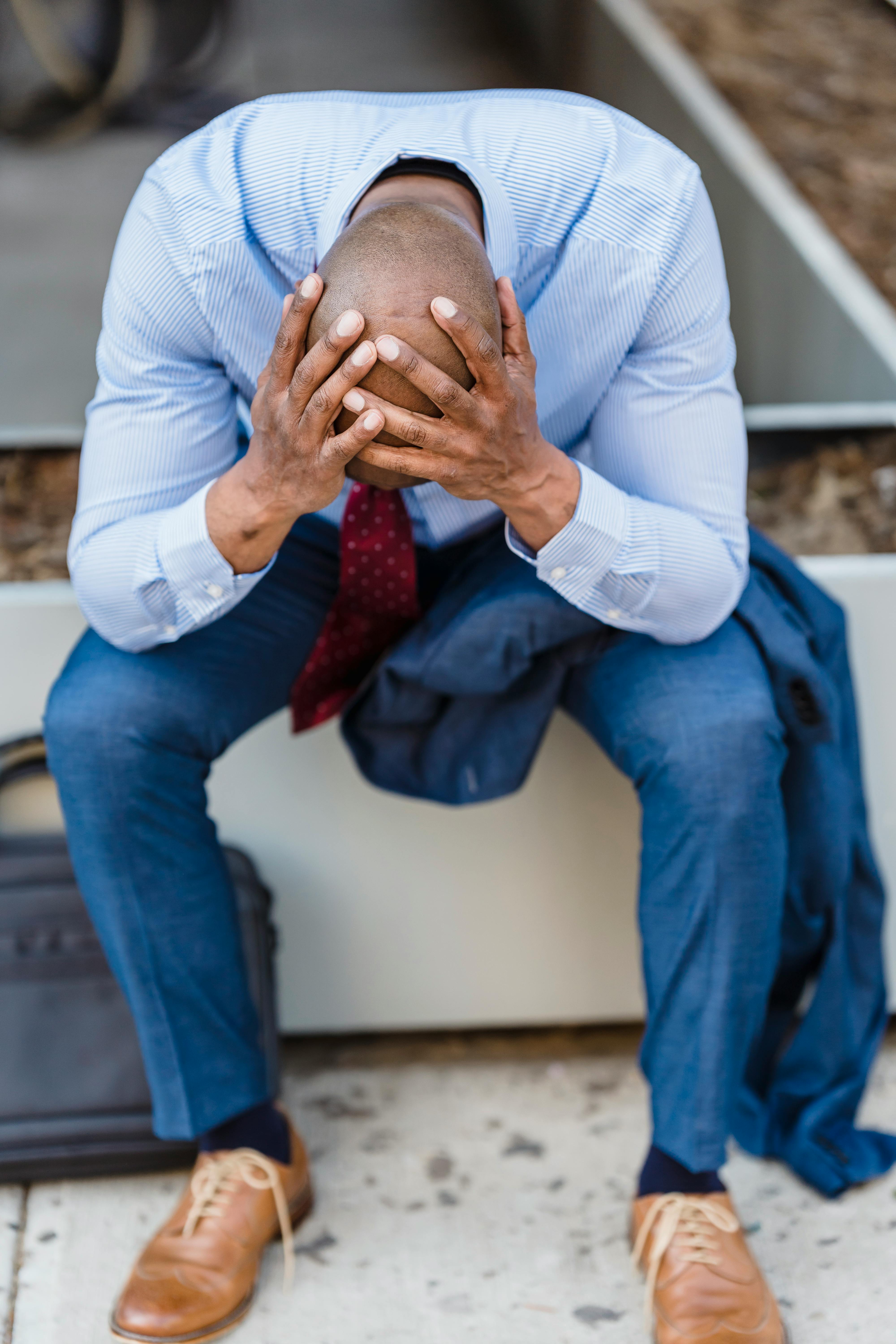 An upset man sitting and holding his head while bent over | Source: Pexels