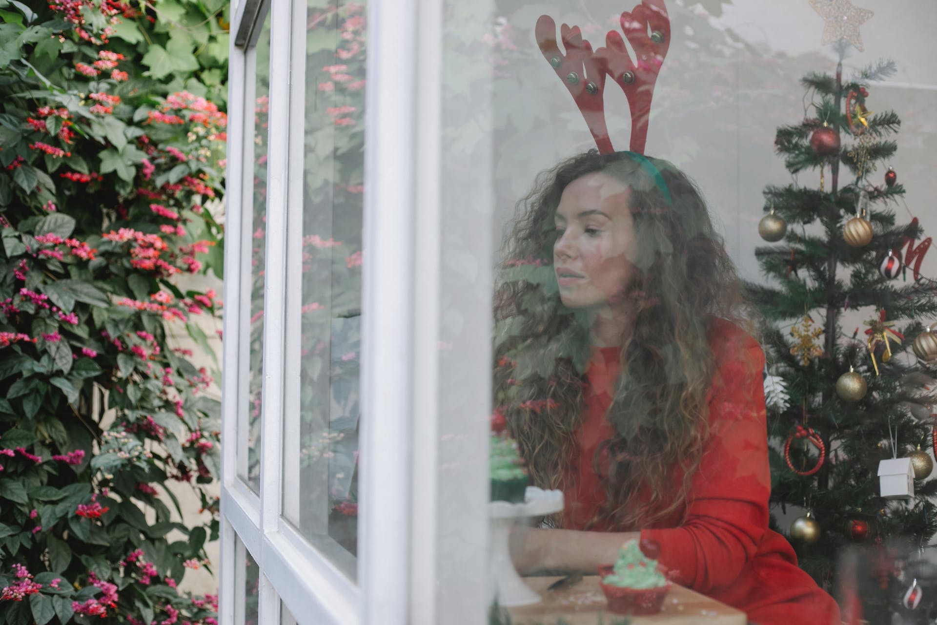 A woman dressed as a reindeer sitting beside a Christmas tree and looking outside | Source: Pexels