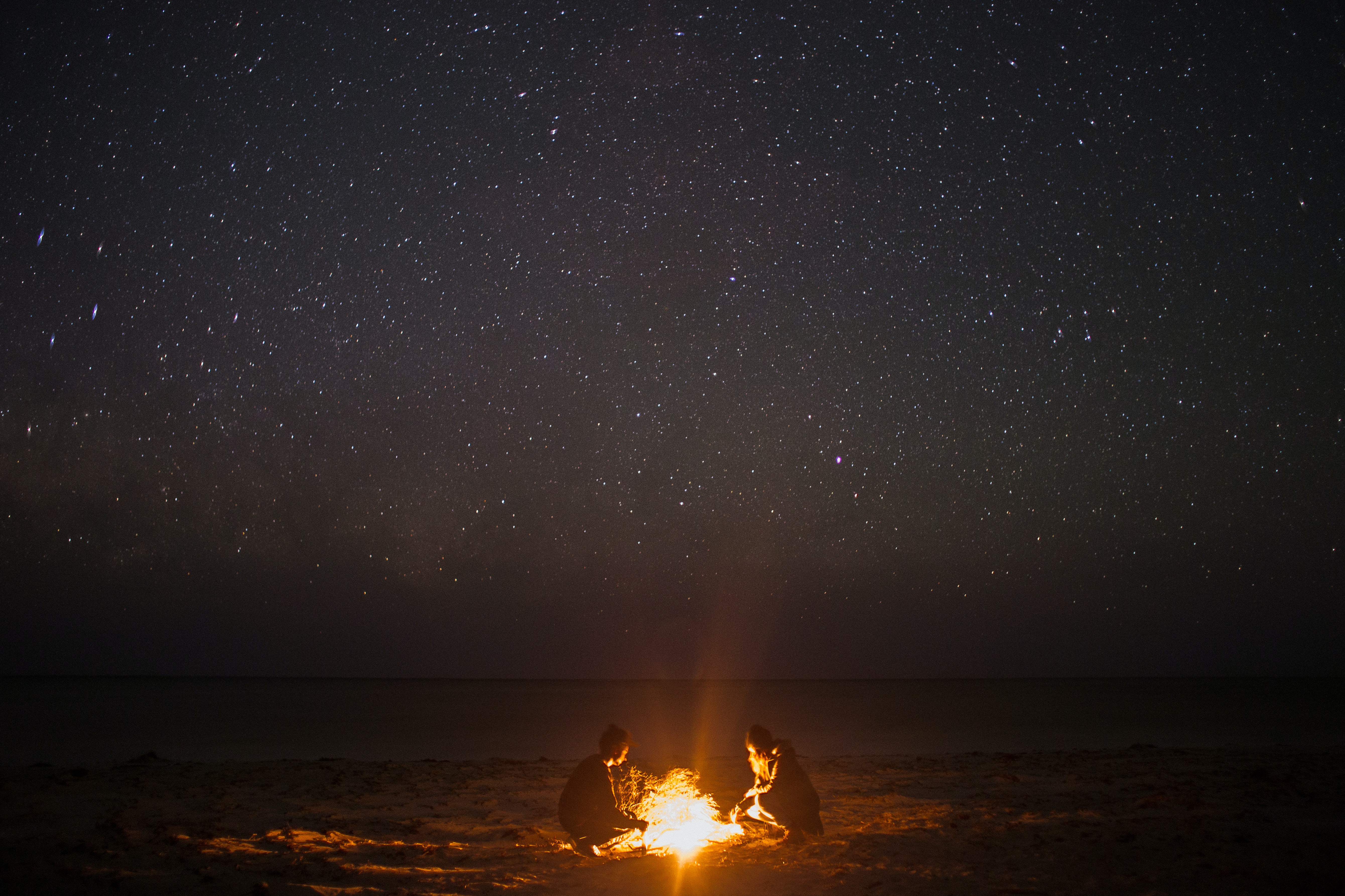 A couple sitting on the beach by a fire. | Source: Pexels