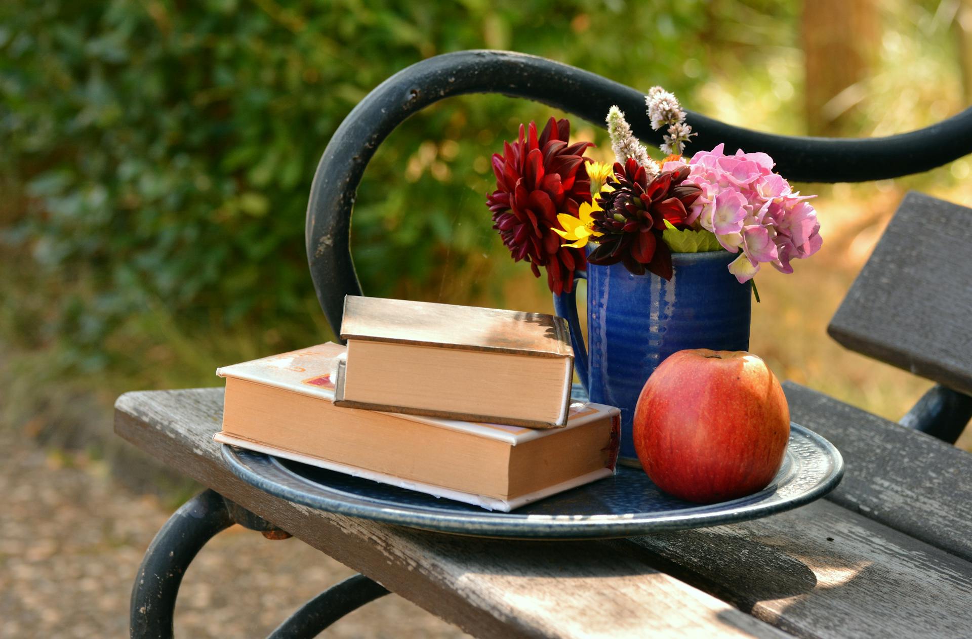 Two books placed on top of each other beside a flower vase and a red apple | Source: Pexels