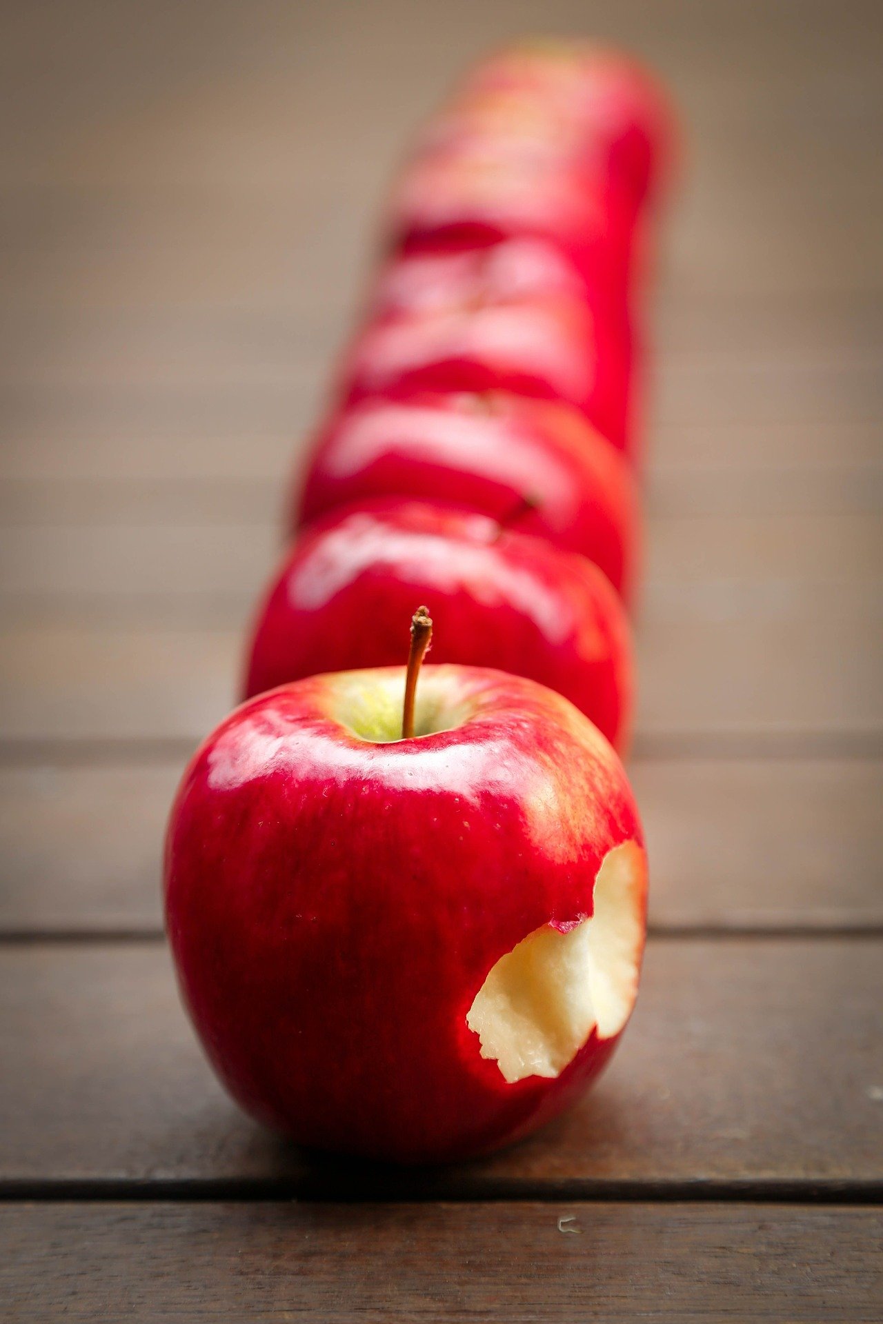 Apples placed on a table in a straight line with the first one featuring bite marks | Photo: Pixabay/Tracy Lundgren