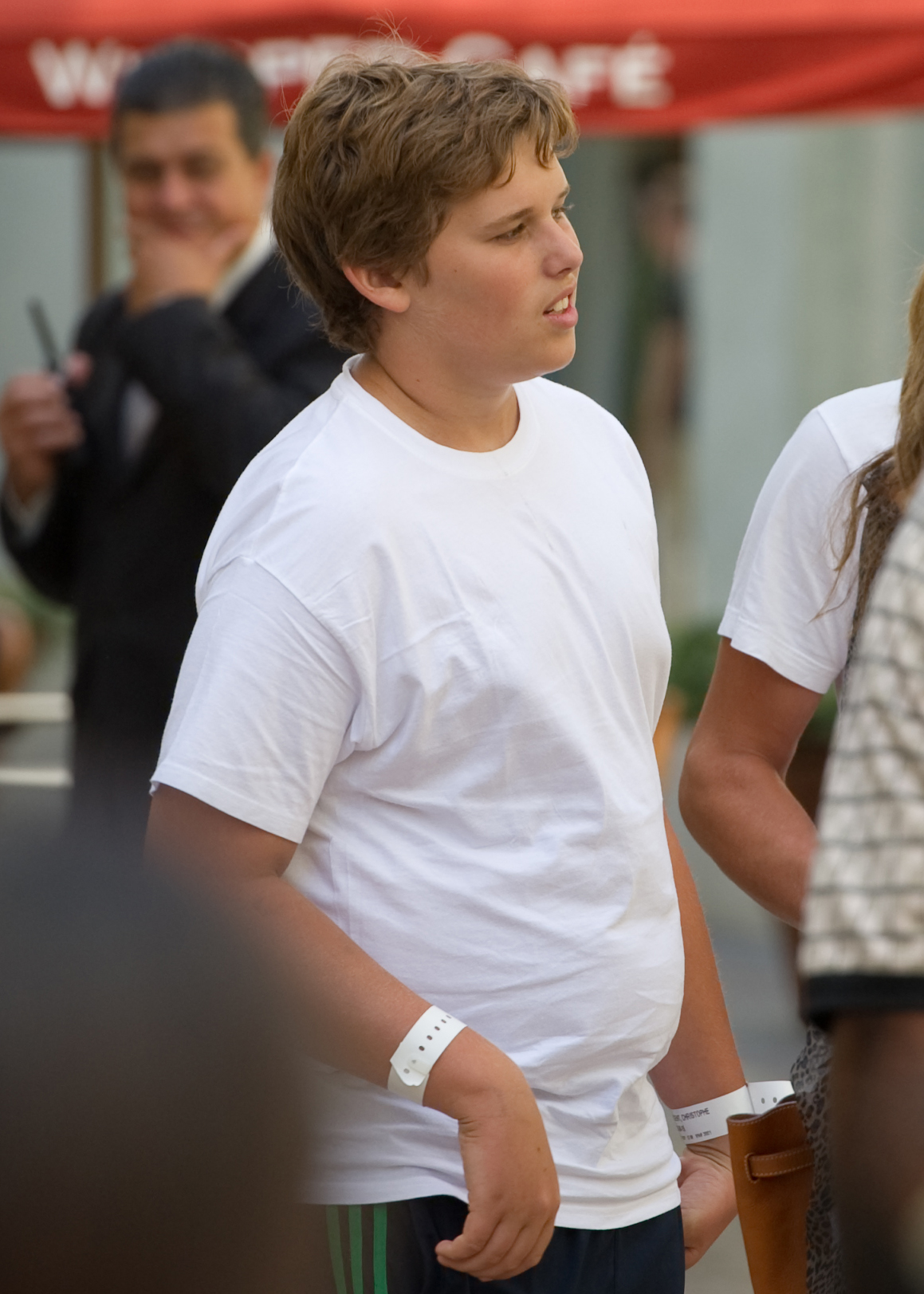 Christopher Schwarzenegger is seen at The Grove in Los Angeles on July 27, 2011. Wearing a simple white t-shirt and dark athletic pants, he appears in his early teens, standing among others in a relaxed setting.