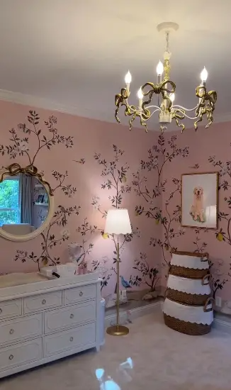 A delicate and sophisticated nursery setup with floral mural wallpaper, a classic white dresser, and a playful chandelier captures the warmth and elegance Alex Drummond envisioned for her daughter’s room. Each detail reflects a timeless charm. | Source: Instagram/alexmariedrum