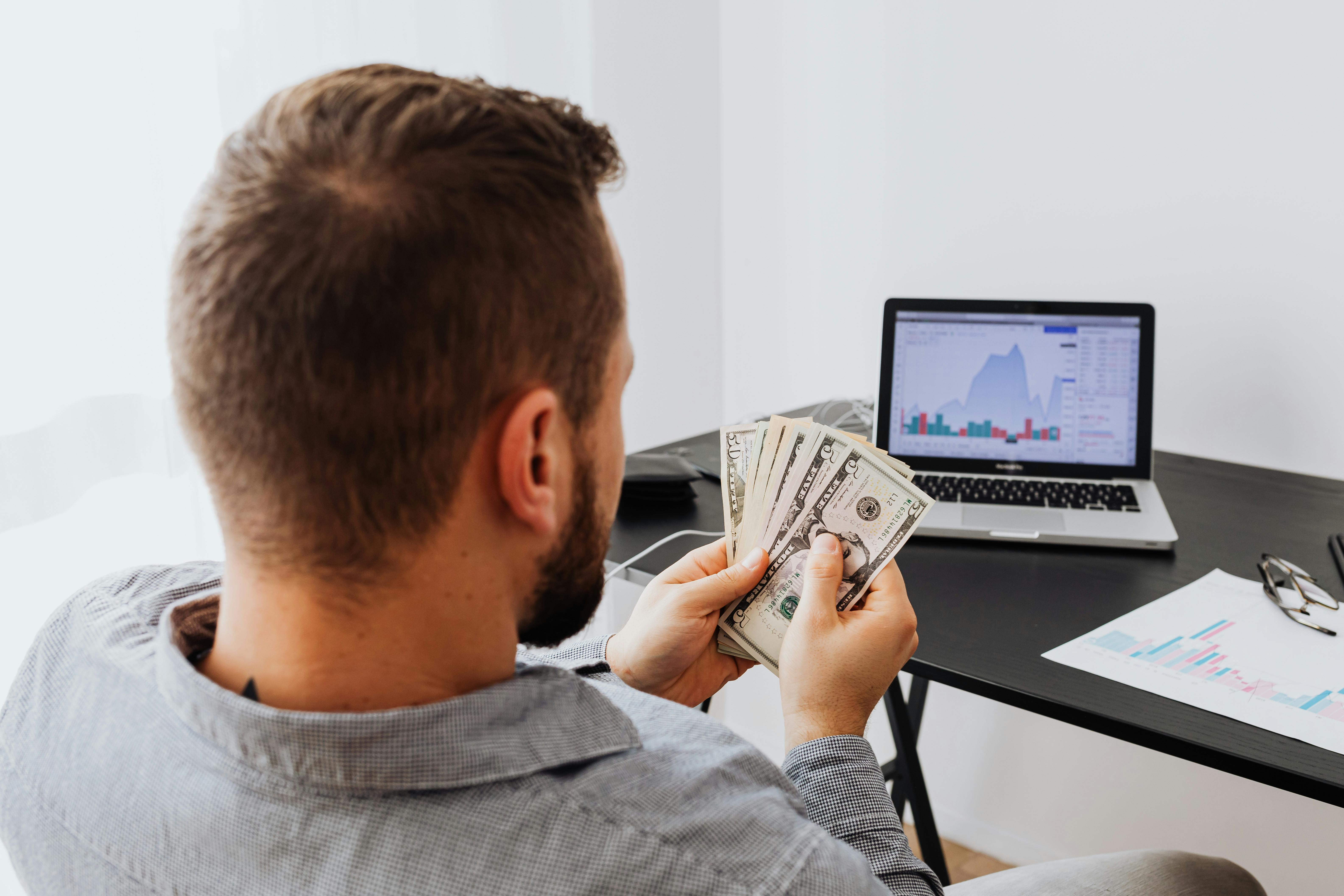 A man sitting in front of a laptop counting money | Source: Pexels
