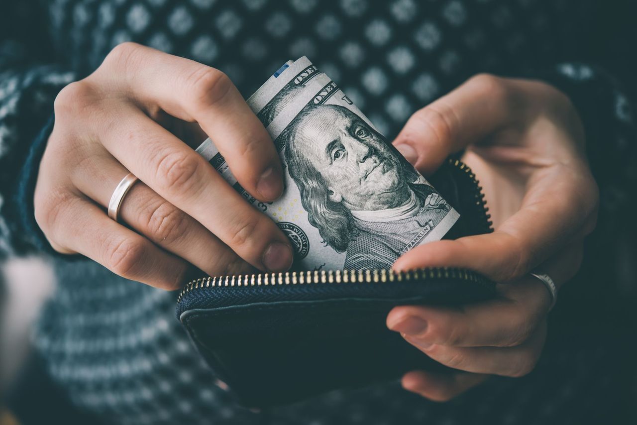 A woman pulls dollar bills from her wallet. | Source: Shutterstock