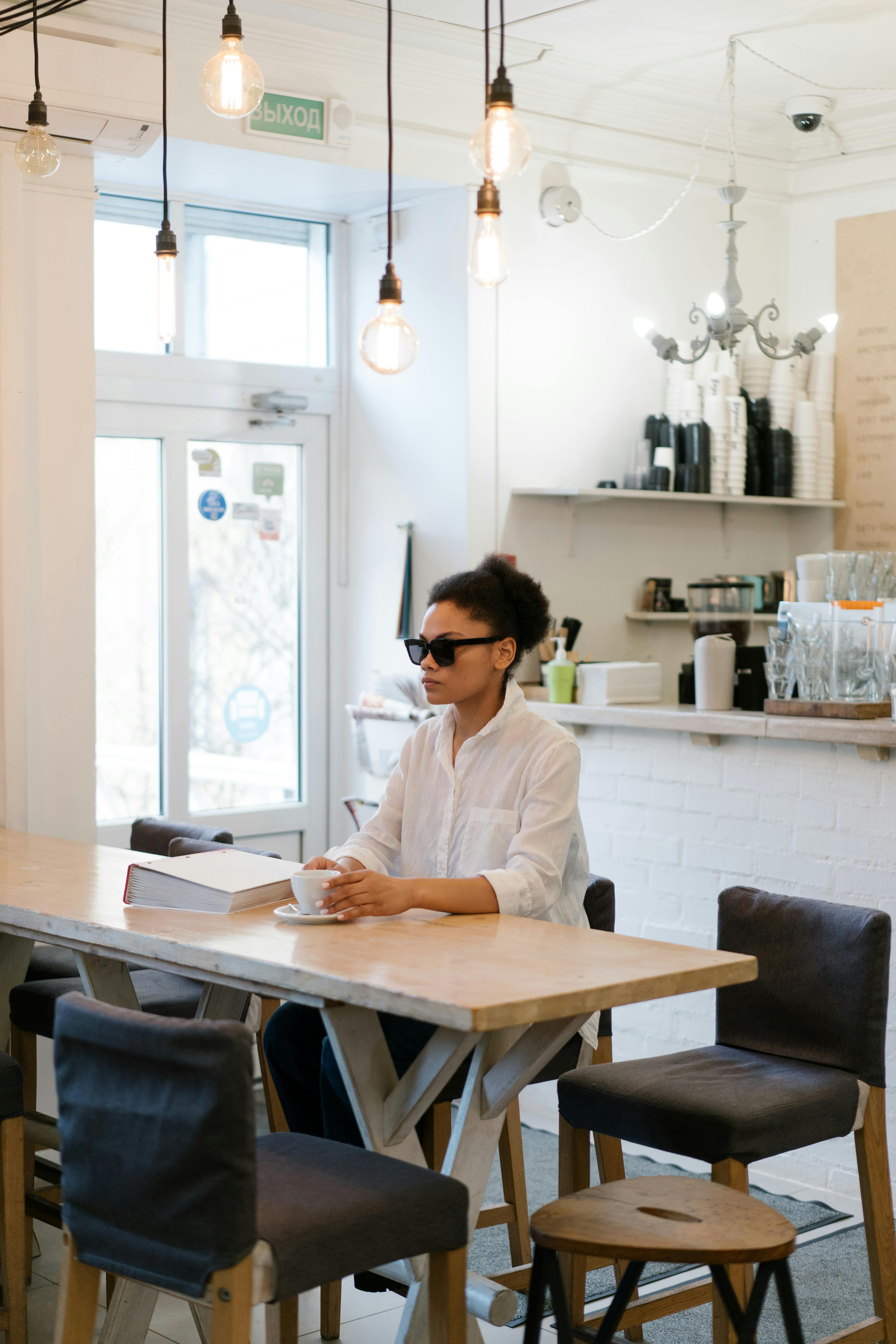 A woman wearing sunglasses sitting at a table in a café | Source: Pexels