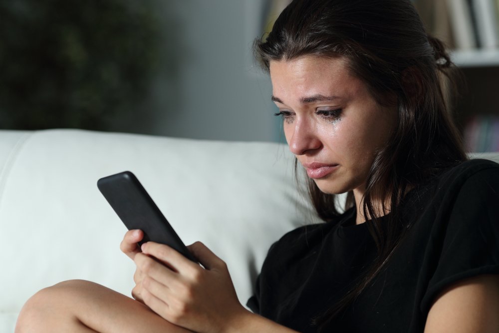 Eine Frau die ihr Handy hält und weint. | Quelle: Shutterstock