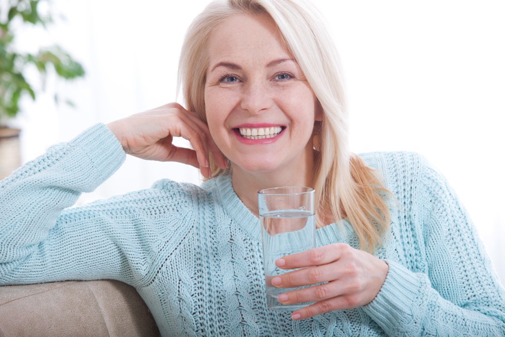Mujer sonriente con un vaso de agua. | Foto: Shutterstock