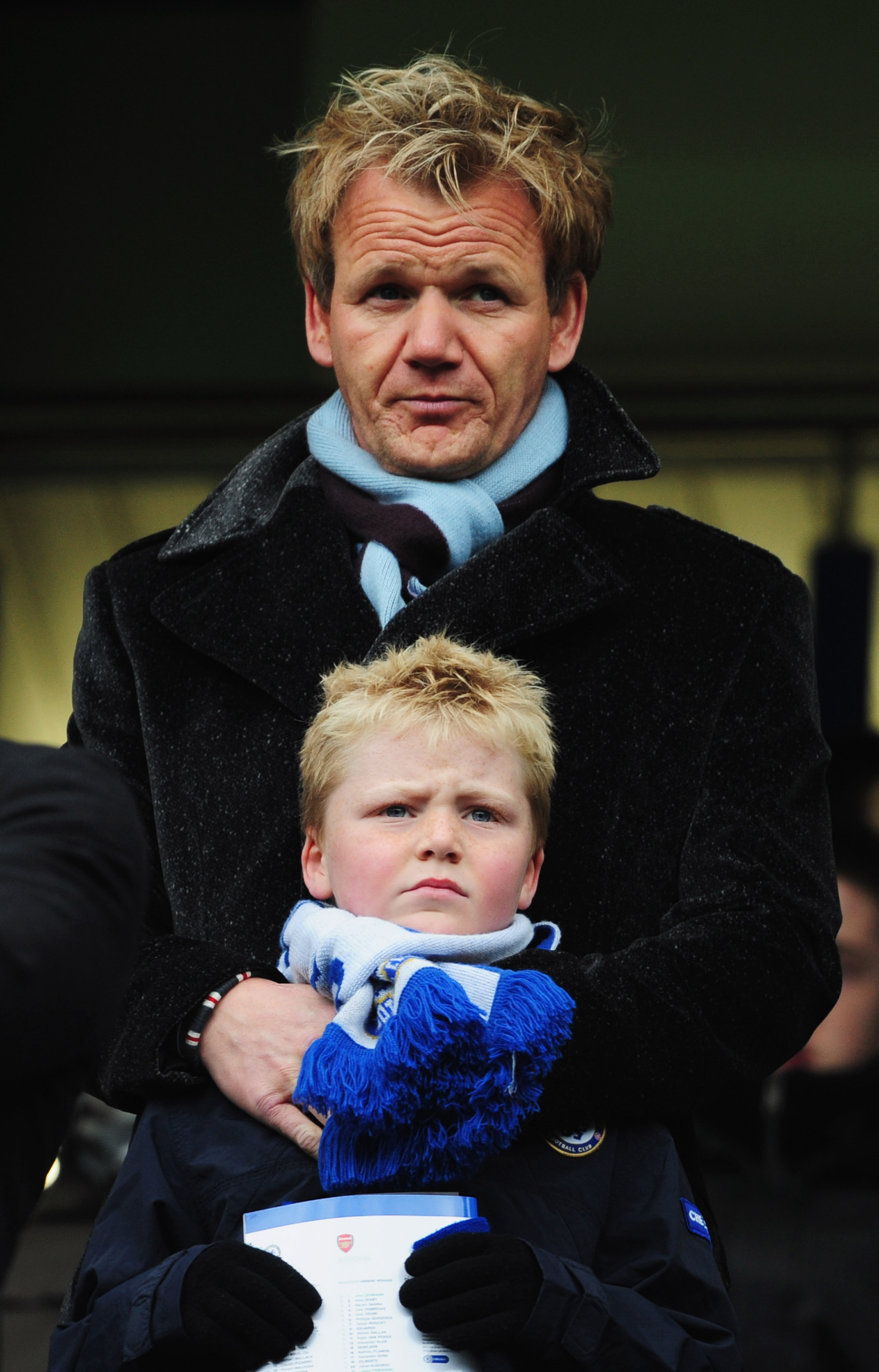 A young Jack Ramsay stood in front of his father as the pair attended the Premier League match between Chelsea and Arsenal at Stamford Bridge on March 23, 2008. Wrapped in a blue scarf and gloves, Jack's serious expression reflected the intensity of the day, while Gordon's protective stance suggested the quiet bond they had long shared.