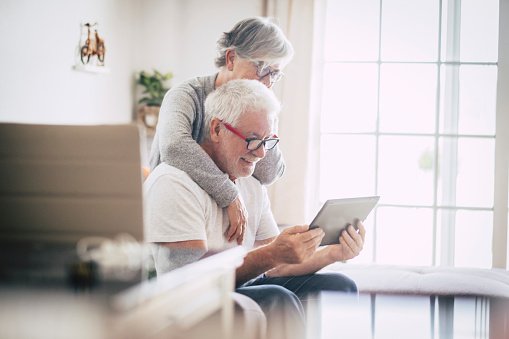 Un couple de personnes âgées souriant et regardant la tablette à la maison. | Photo : Getty Images